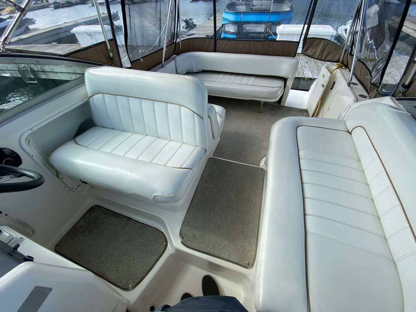 .Cockpit of a boat with white cushioned seats and beige flooring, docked at a marina. Sea Ray 270 Sundancer. 