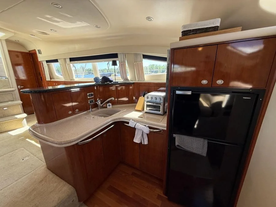 Cherry wood kitchen with a small countertop stove, sink, black refrigerator, and large windows by the water. on a Sea Ray luxury yacht.