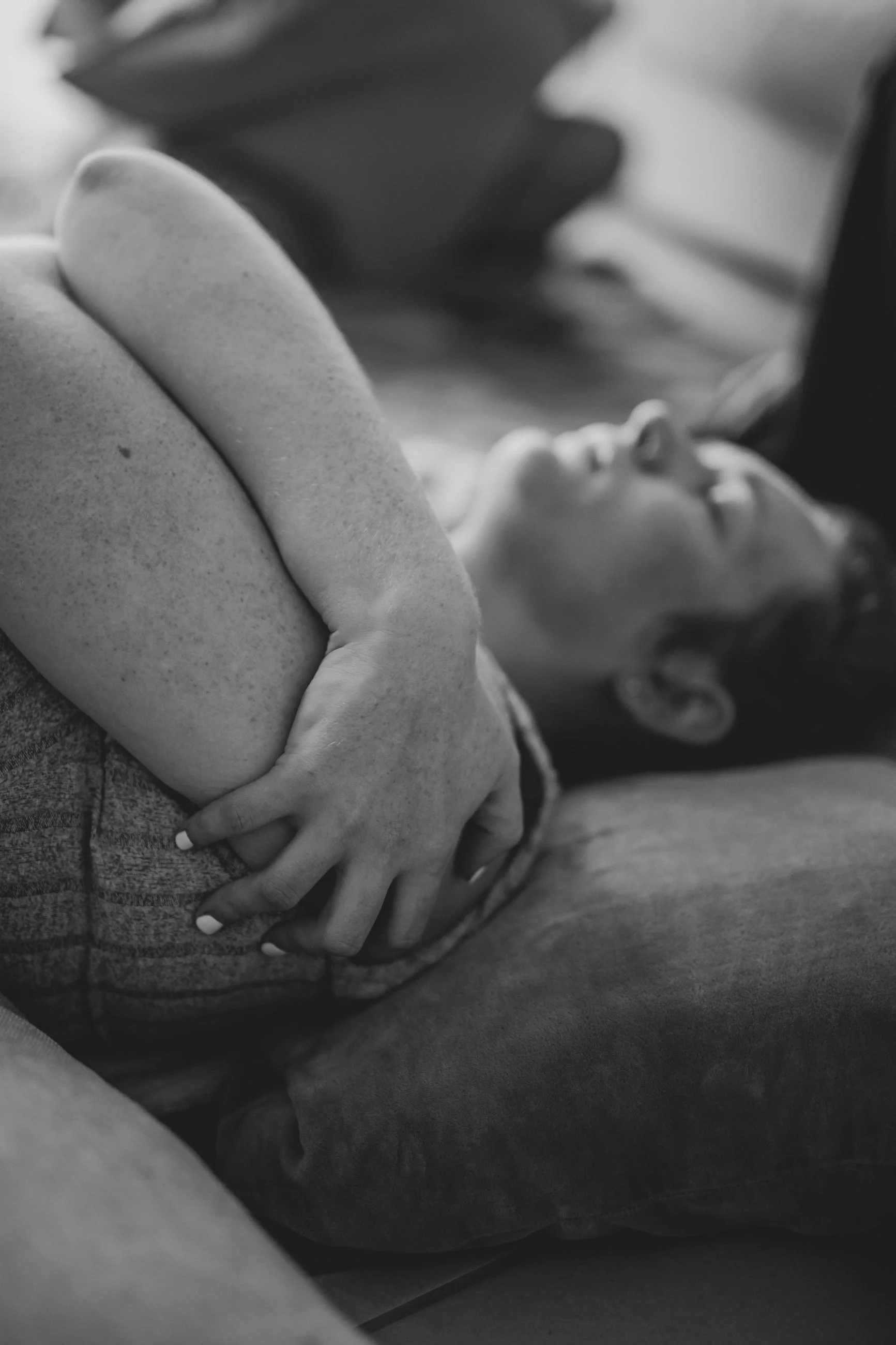 A woman with freckles laying on a couch, cuddling a child with short hair and closed eyes, in black and white.