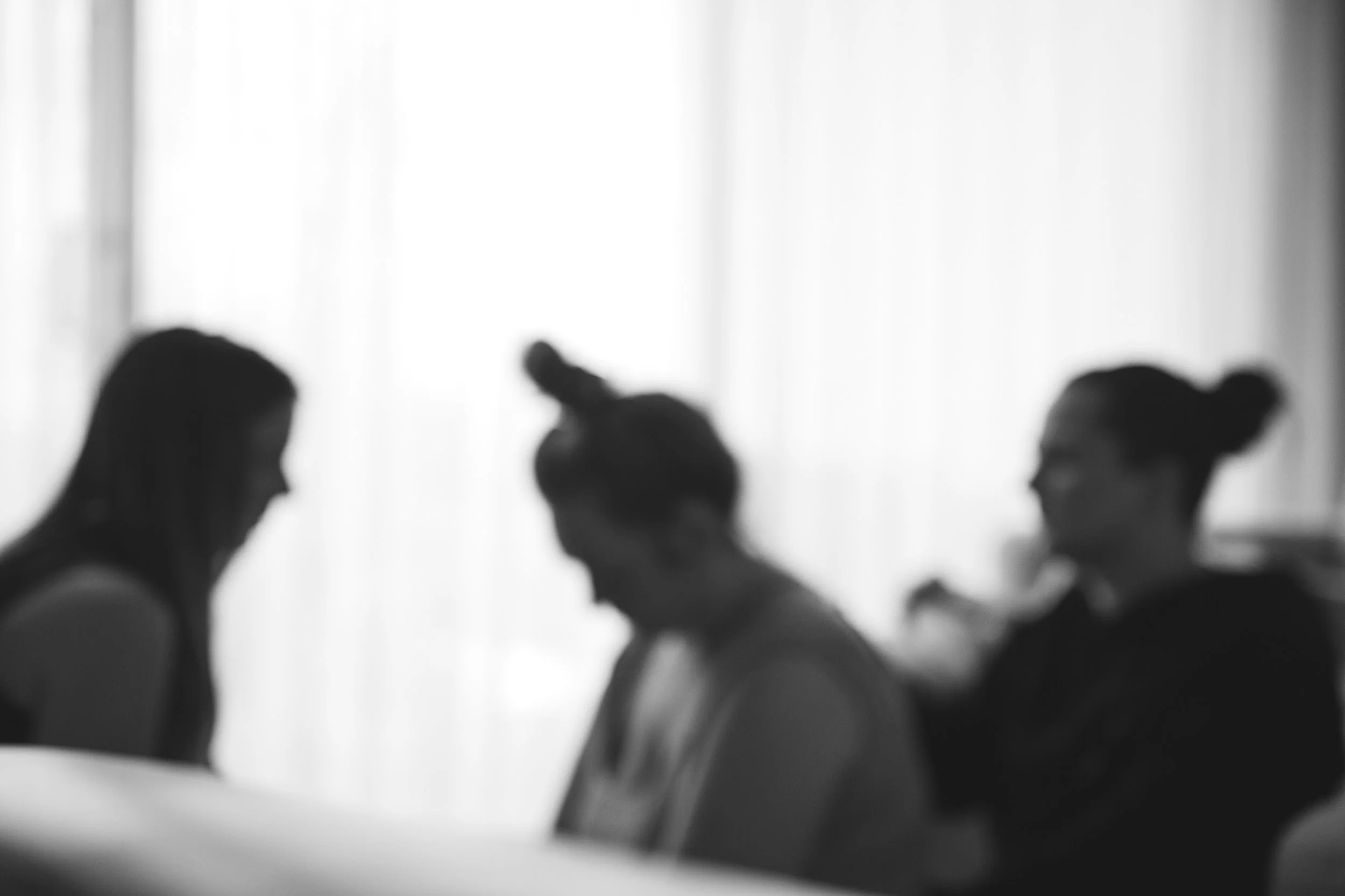 Silhouettes of three women sitting and engaging in conversation, in black and white with blurred background.