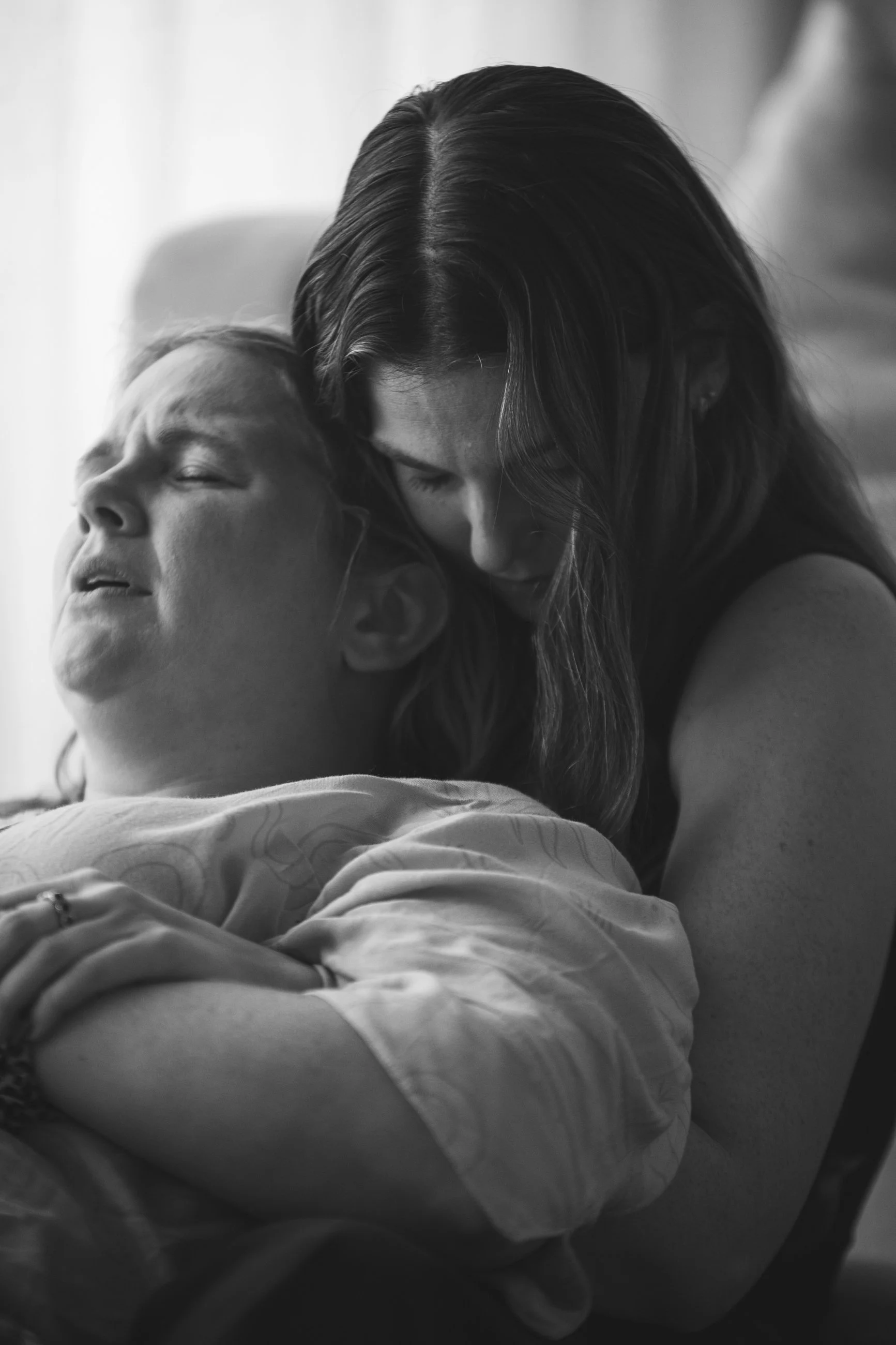 A woman holding a person in her arms, both with their eyes closed, in an intimate and comforting embrace.