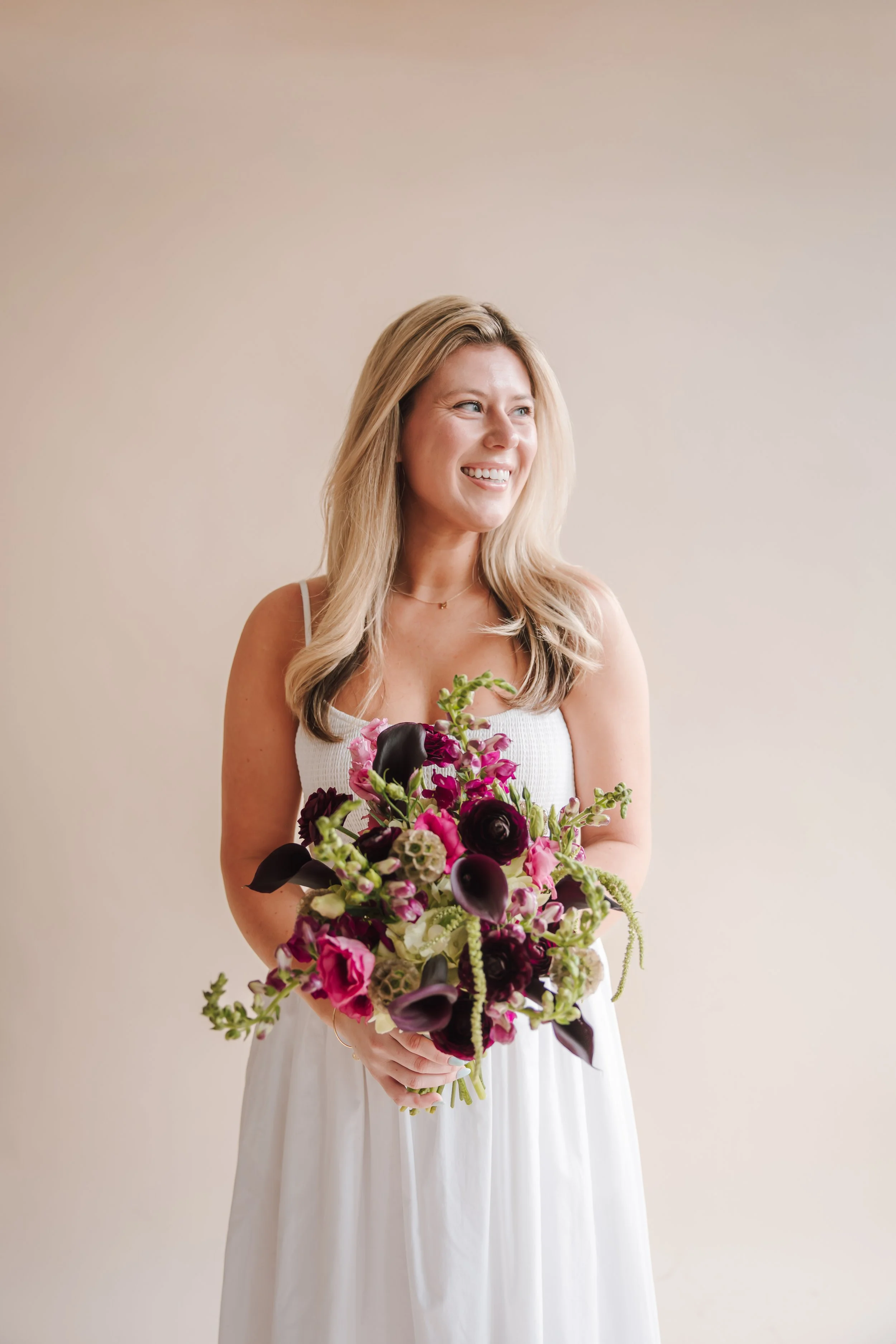 A smiling woman in a white dress holding a colorful bouquet of flowers.