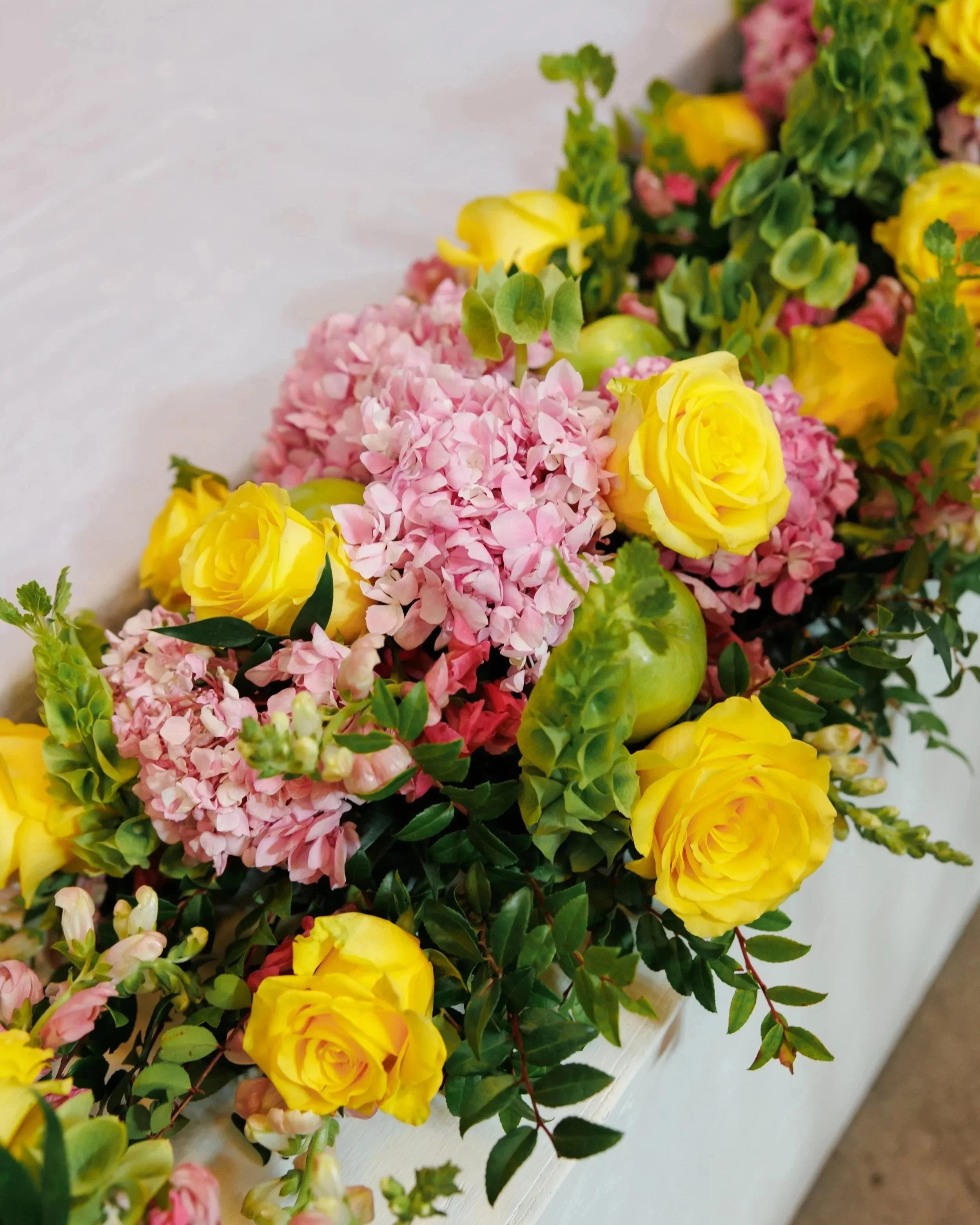A floral arrangement with yellow roses, pink hydrangeas, and greenery.