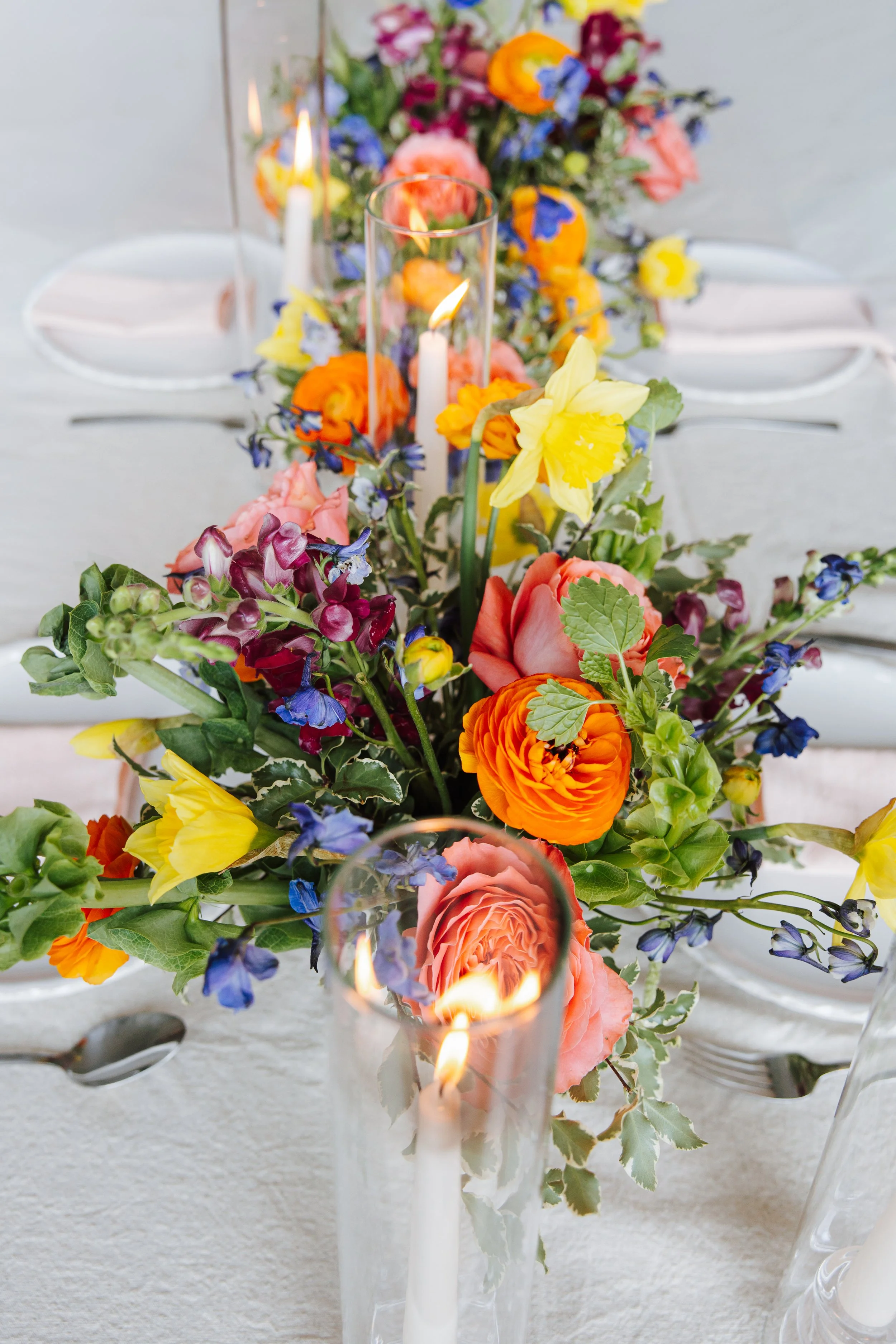 Colorful floral centerpiece with candles on a white table.