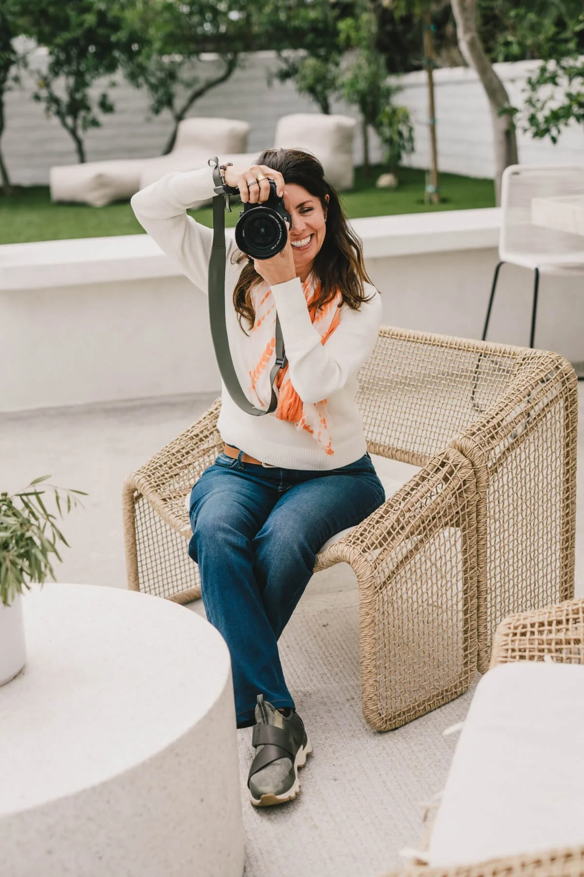 kim morris photographer outside taking picture with her favorite lens in jeans white sweater and orange scarf