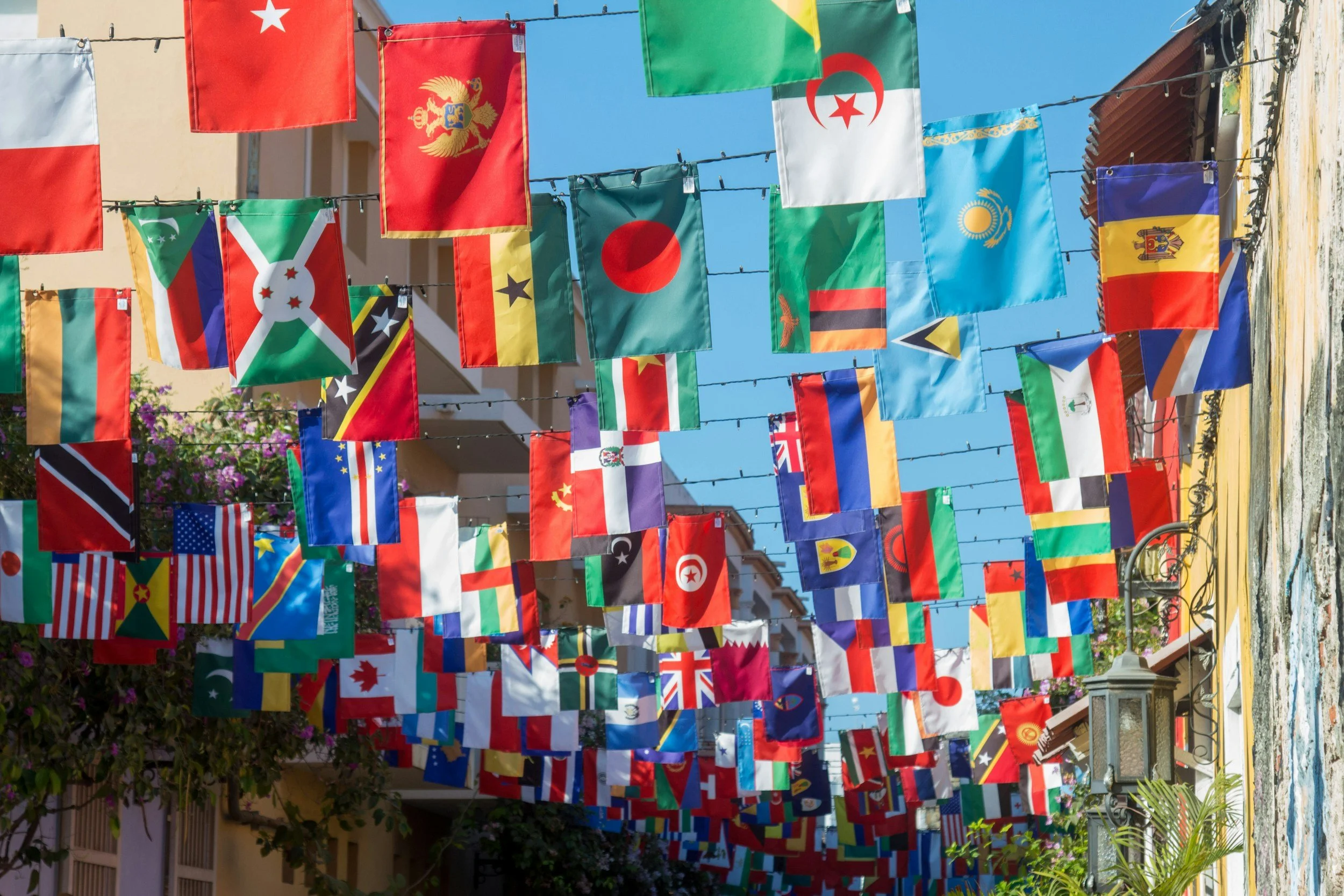 Colorful flags from various countries hanging on strings outdoors on a bright, sunny day.