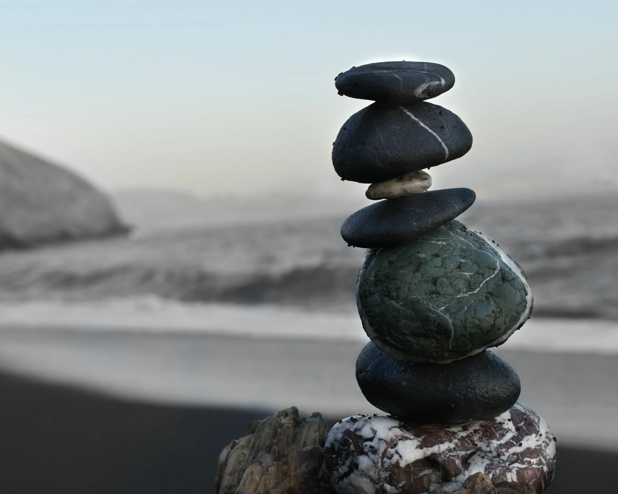 Stacked smooth black and patterned stones on a beach with ocean in the background.
