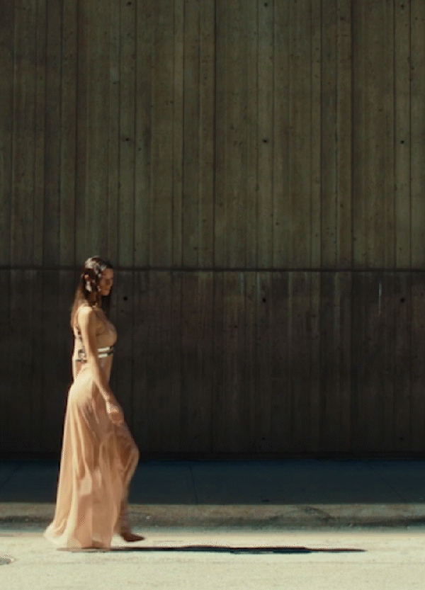 Woman walking in long peach dress with textured concrete wall background.