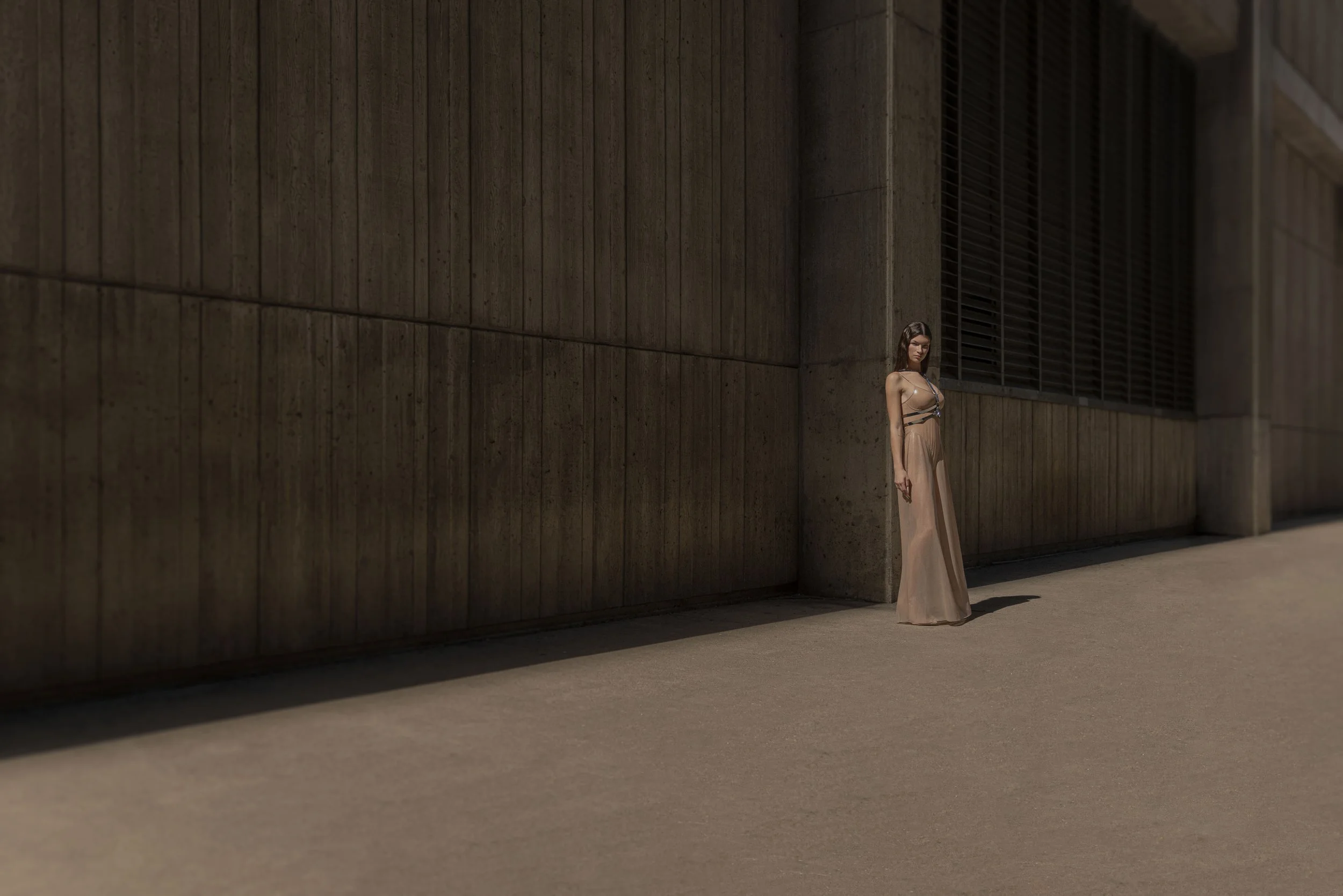 Woman in beige dress standing by a concrete wall in an urban setting