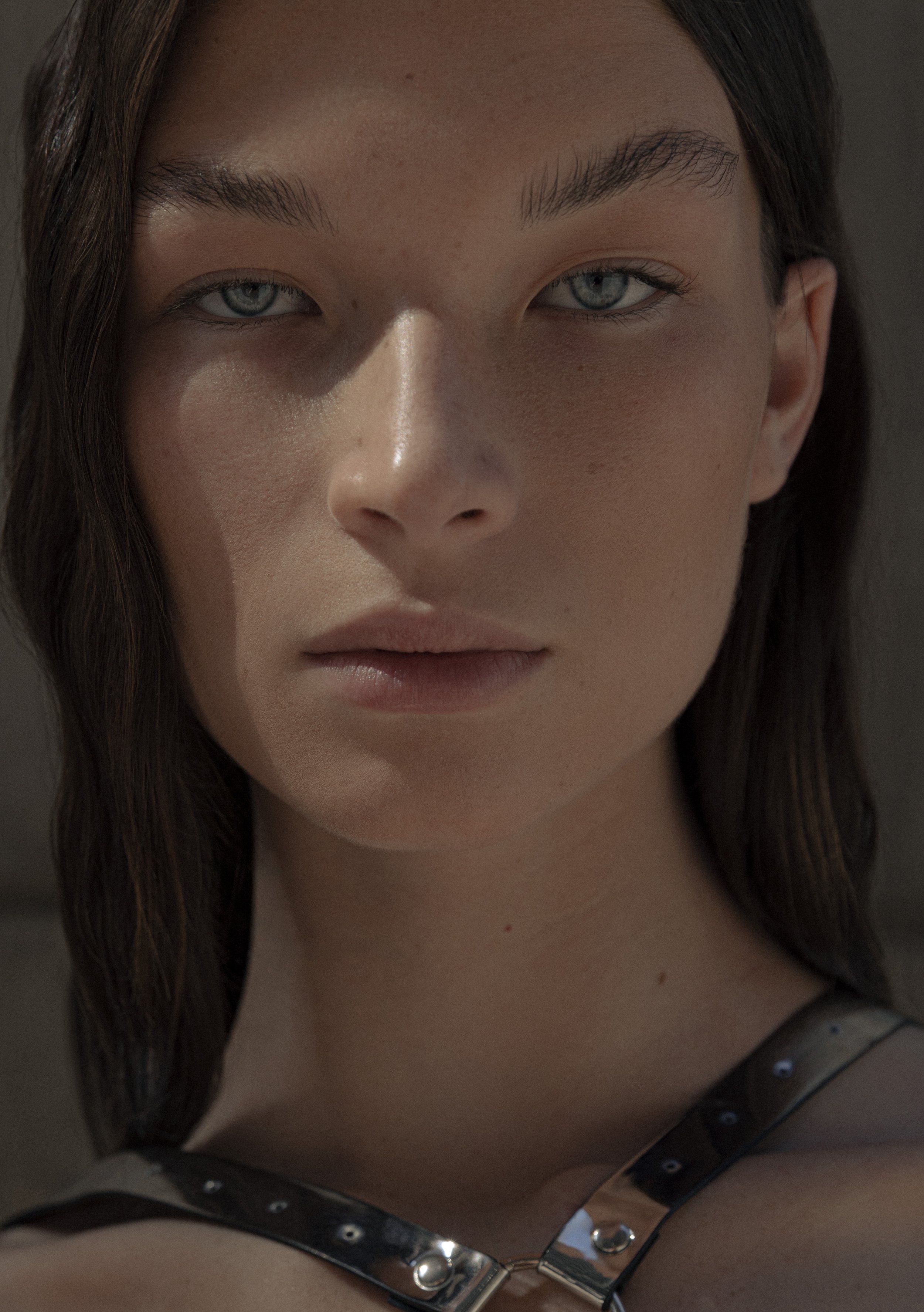 Close-up portrait of a person with straight dark hair, wearing a harness. The background is blurred.