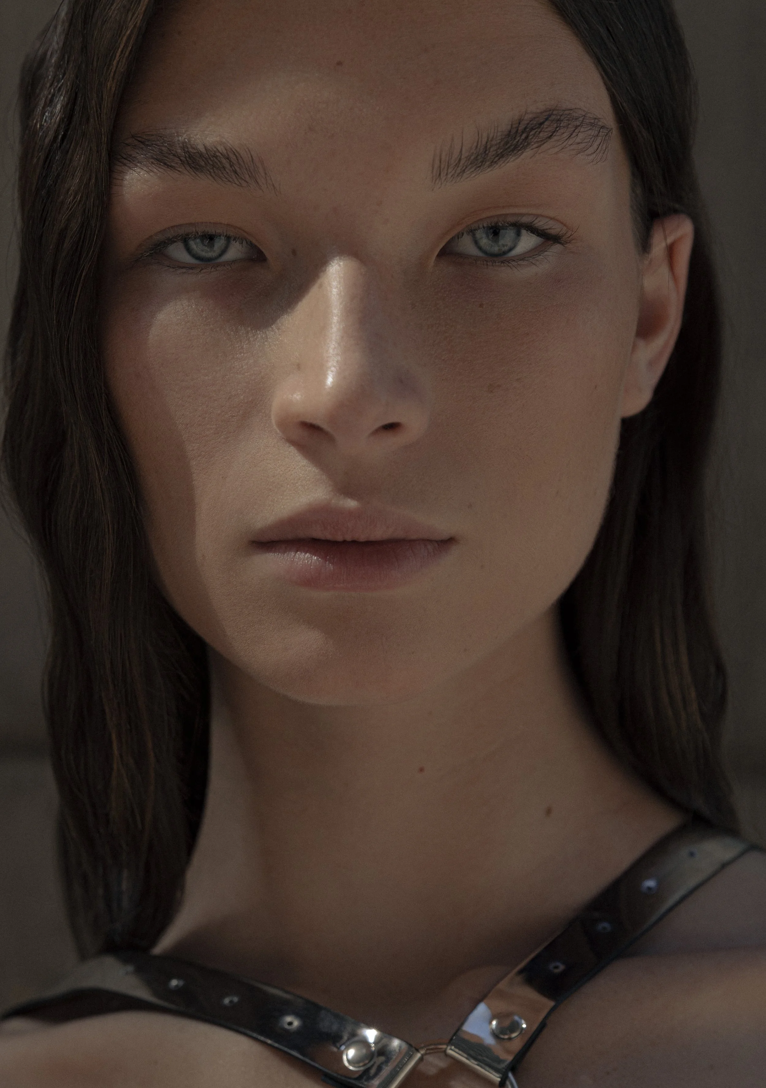 Close-up portrait of a person with straight dark hair, wearing a harness. The background is blurred.
