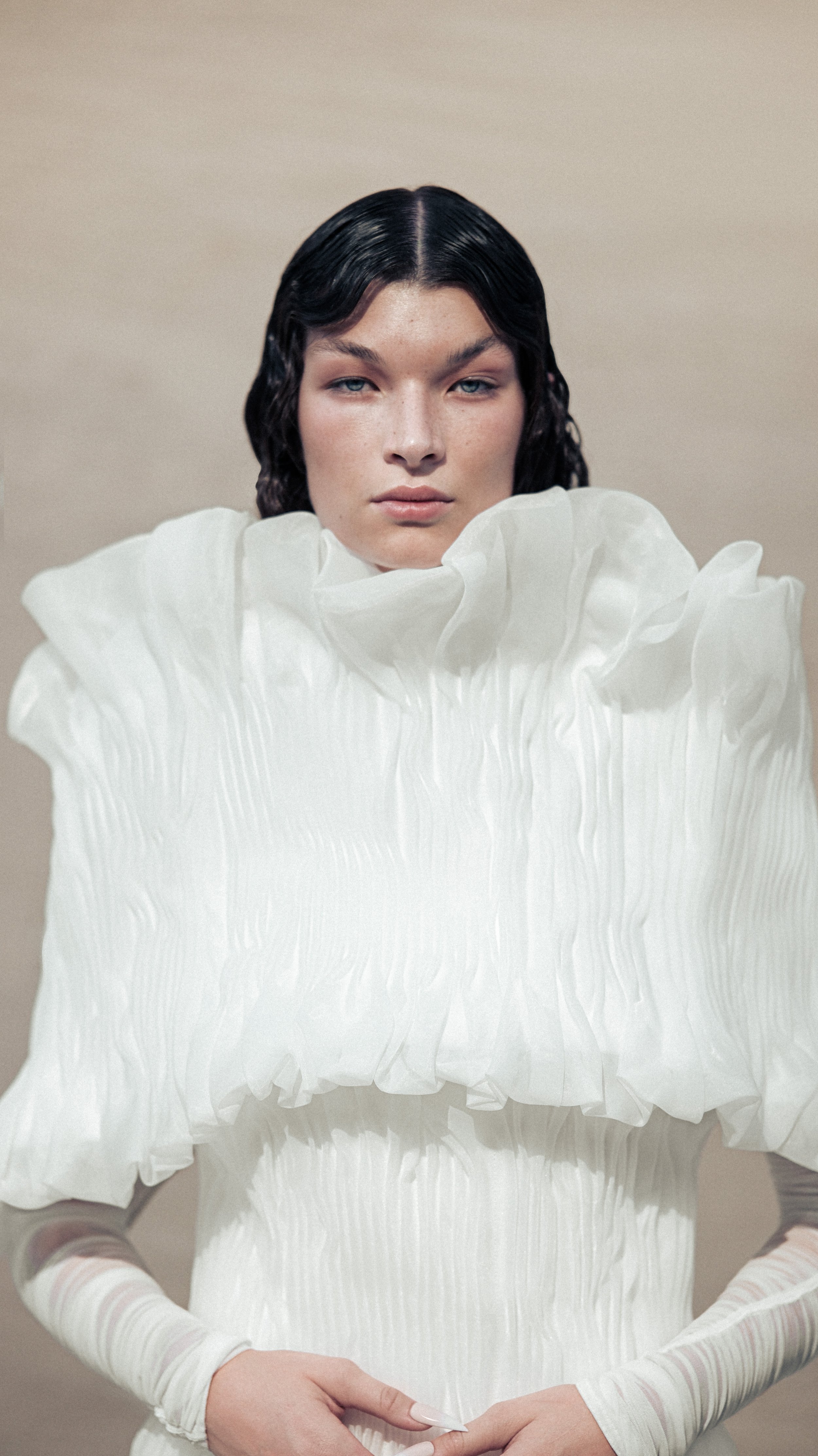 Person wearing a white pleated dress with ruffled collar, standing against a neutral background.