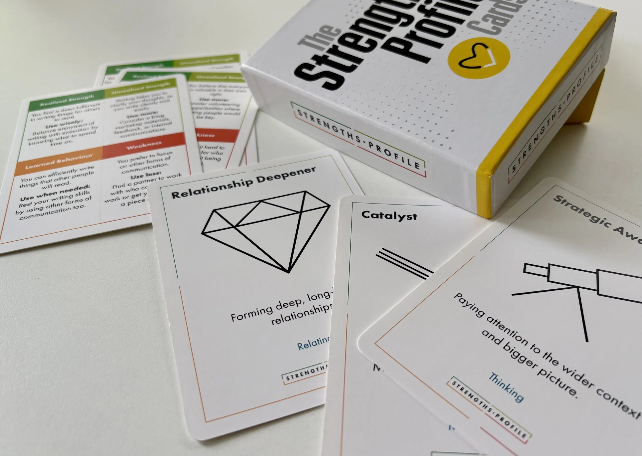 Cards and a box from a Strengths Profile set, including labeled cards such as "Relationship Deepener," "Catalyst," and "Strategic Awareness," on a white surface.