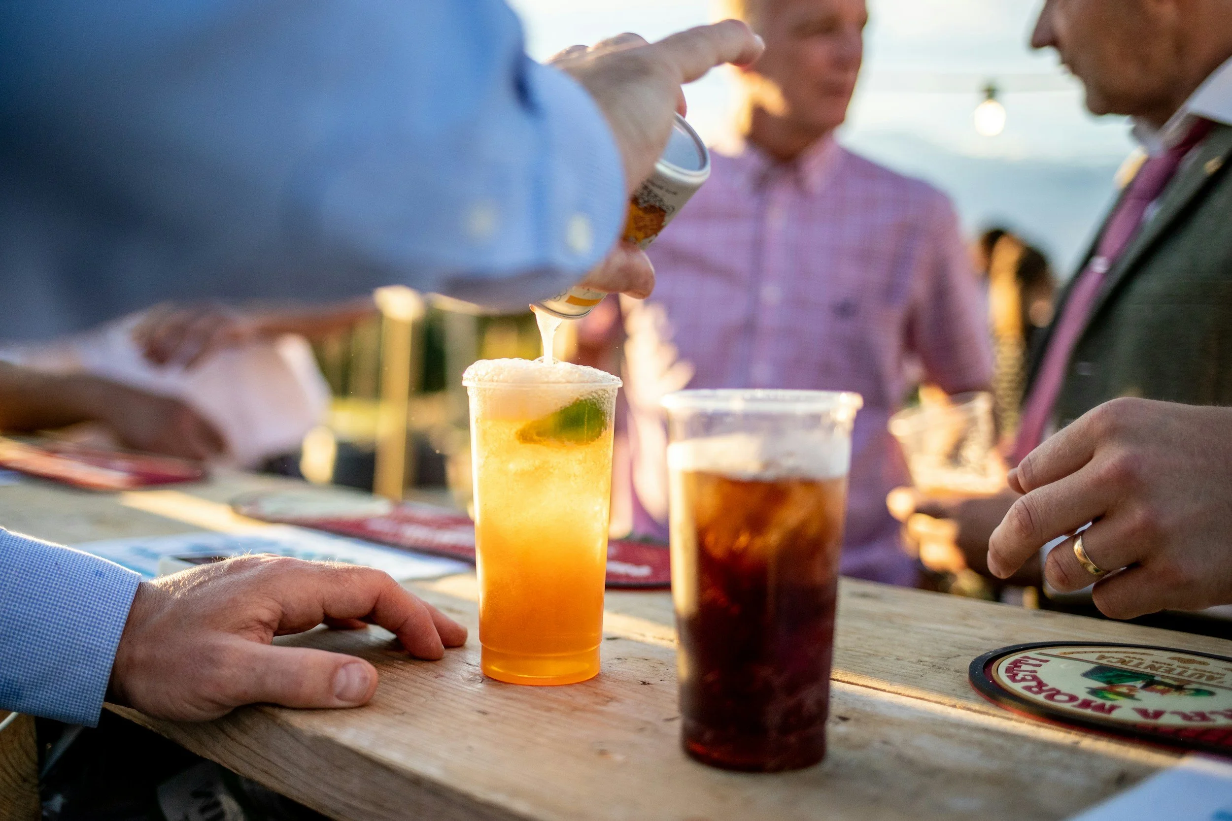 People at an outdoor bar or gathering pouring drinks and socializing during sunset.