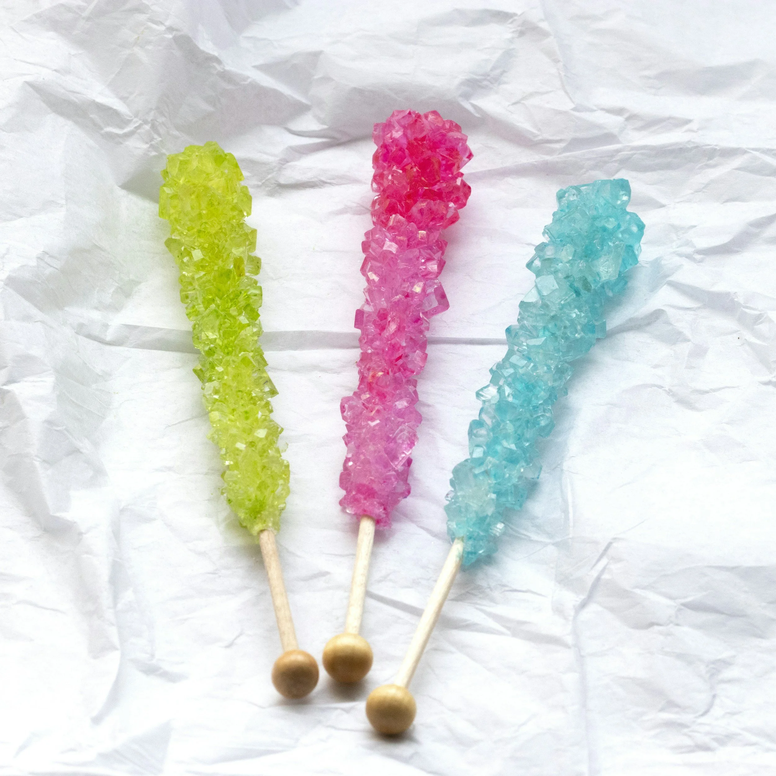Colorful rock candy on sticks placed on crumpled white paper
