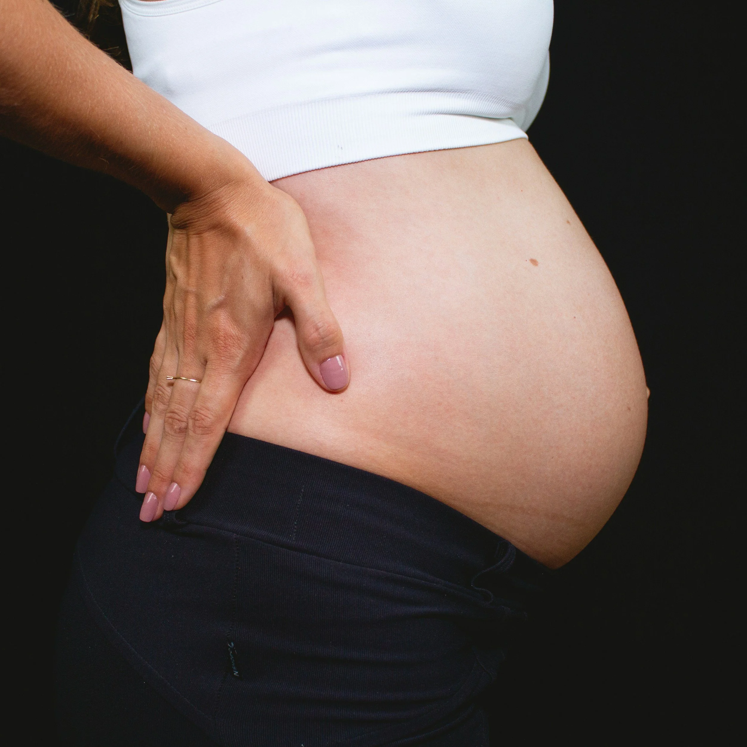 Close-up of a person wearing a white top with their left hand resting on their hip, against a black background.