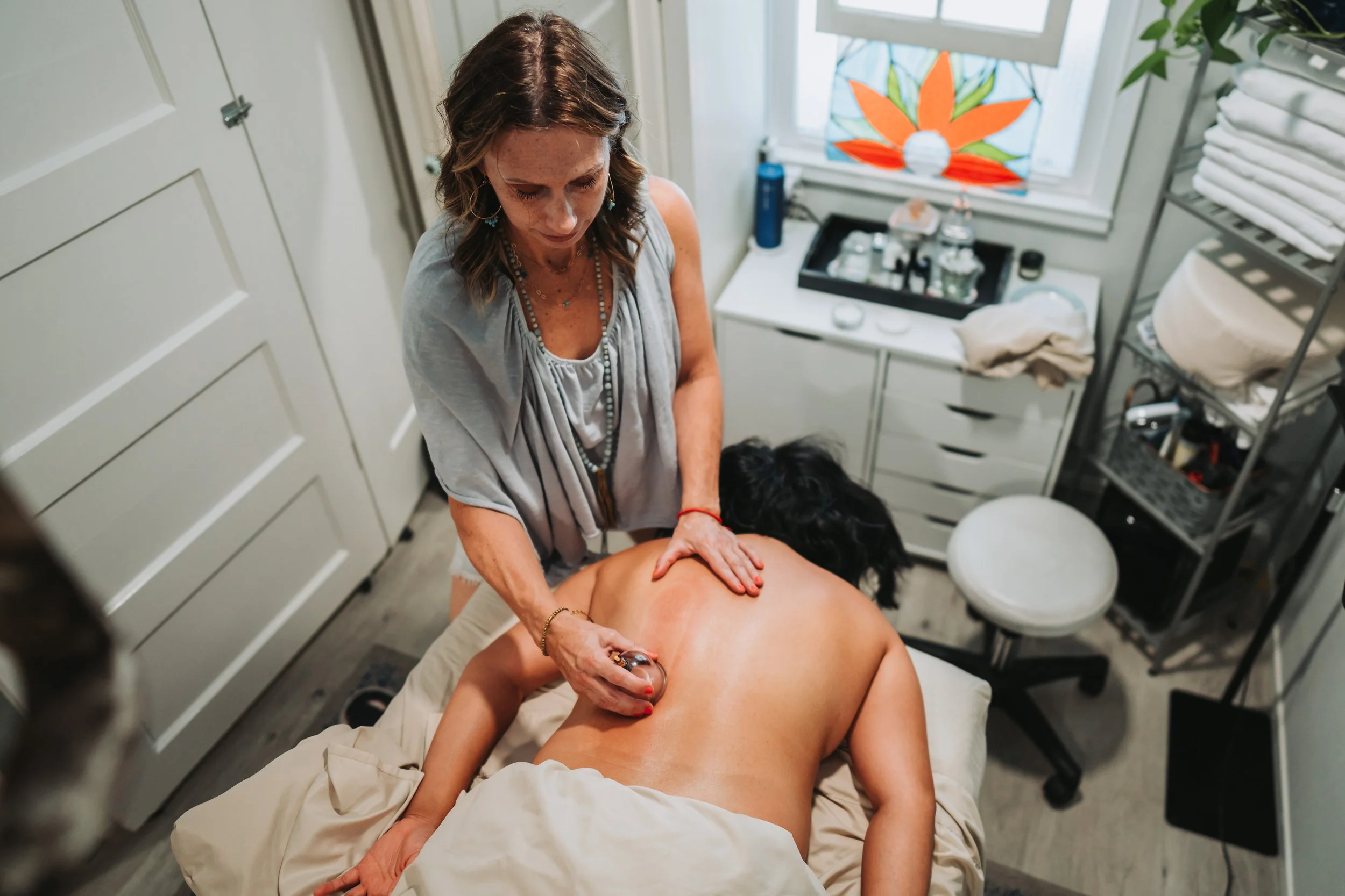 A woman giving a massage to a person lying face down on a massage table in a treatment room.