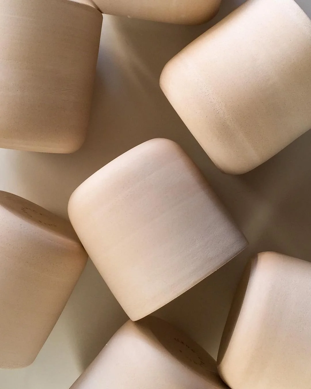 Multiple beige, bisque fired unfinished ceramic cups,  arranged on a surface.