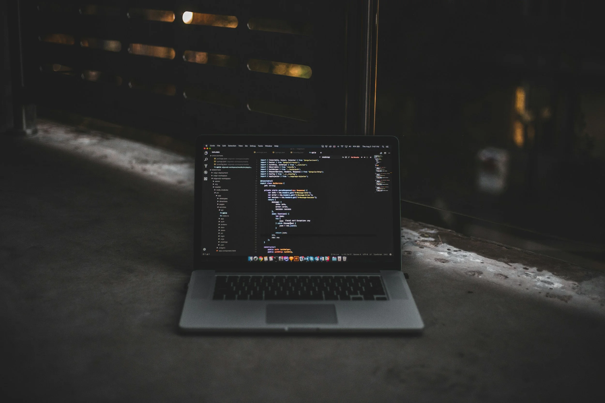Computadora portátil encendida mostrando código de programación en una habitación oscura junto a una ventana.