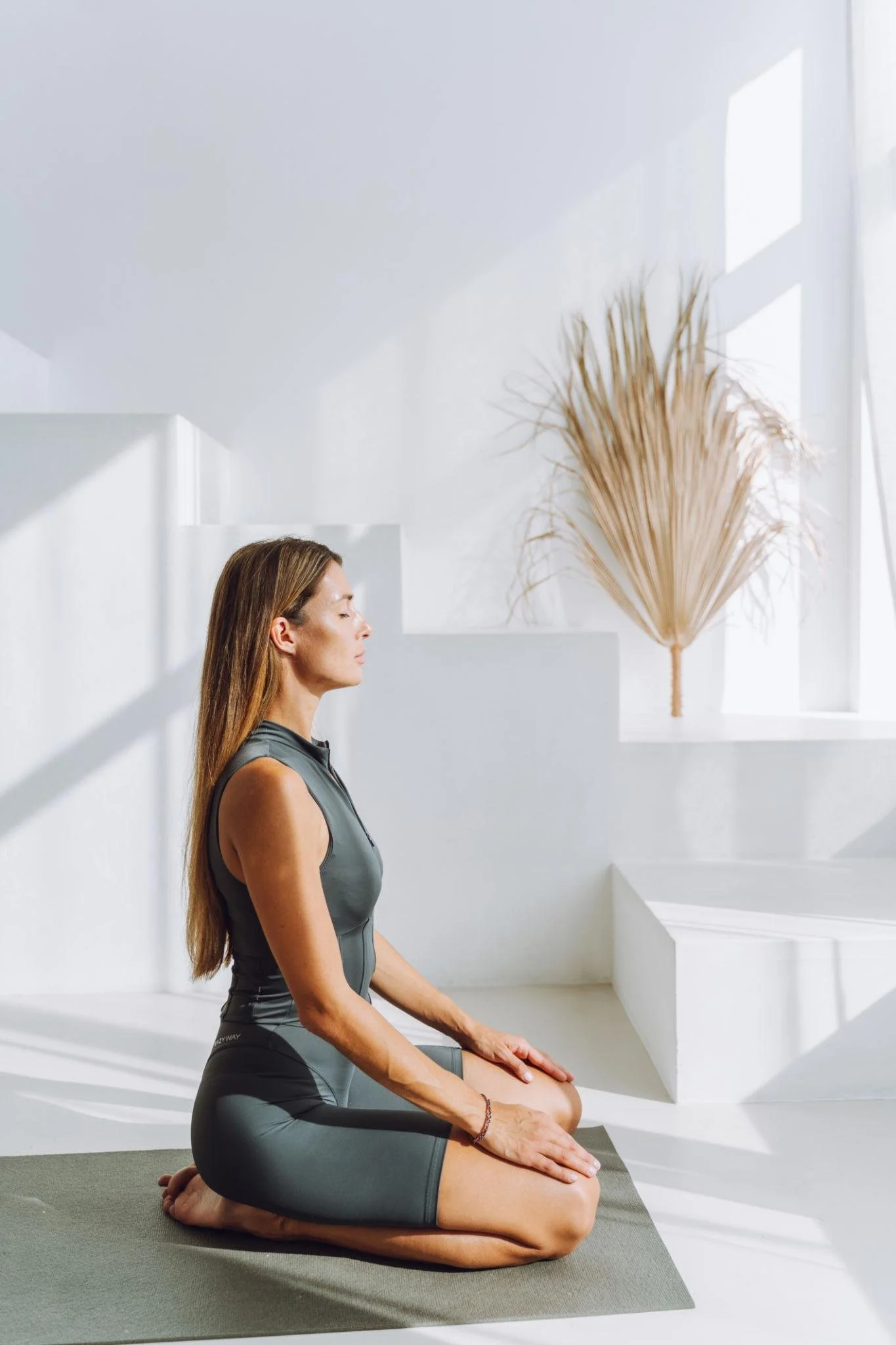 A woman practicing yoga in a bright, minimalistic room with white walls and sunlight streaming in.