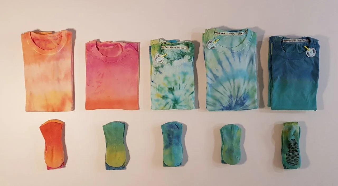 Five folded tie-dye T-shirts and five pairs of matching socks arranged on a white surface.
