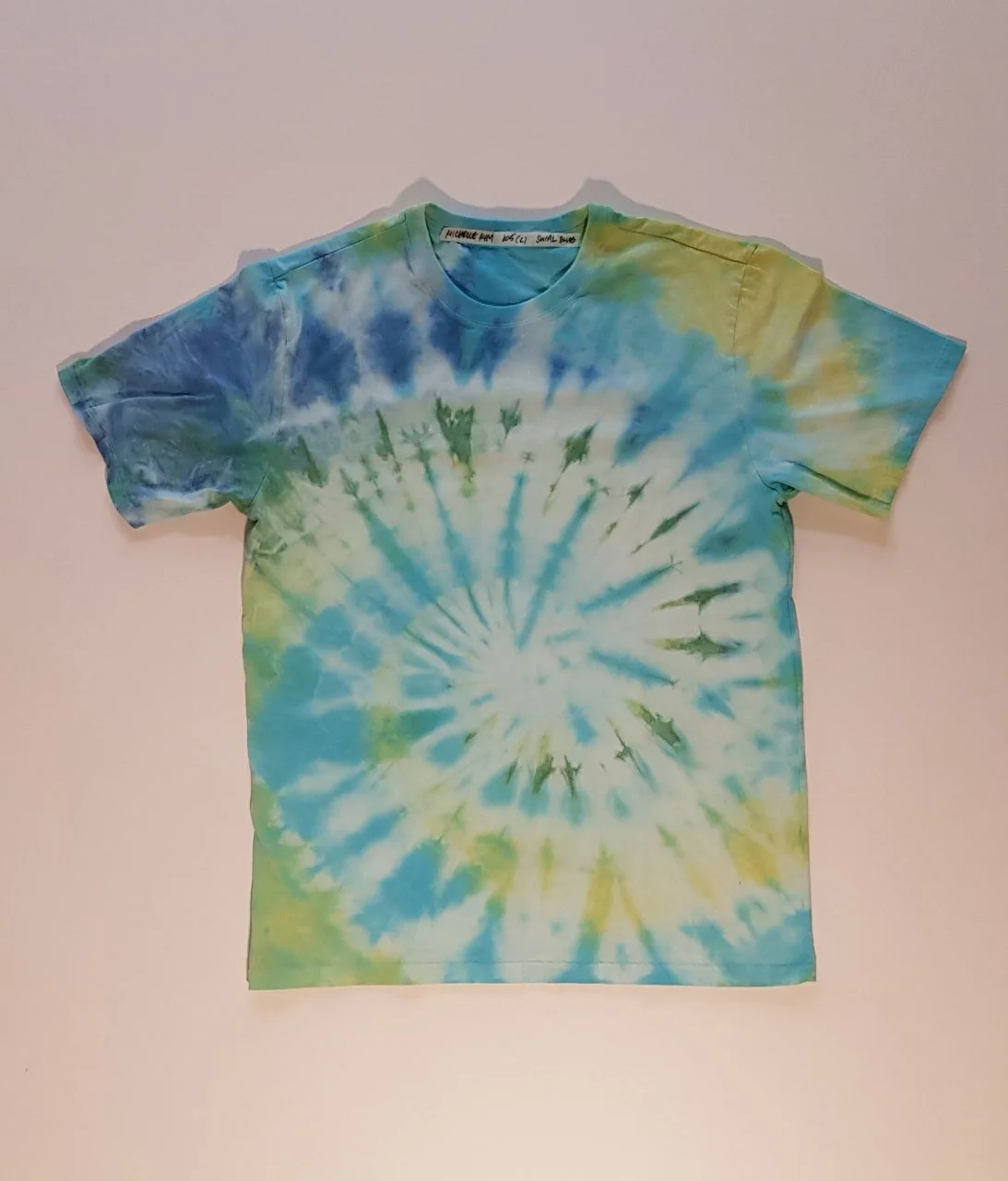 A tie-dye T-shirt with a spiral pattern in shades of blue, green, and yellow.
