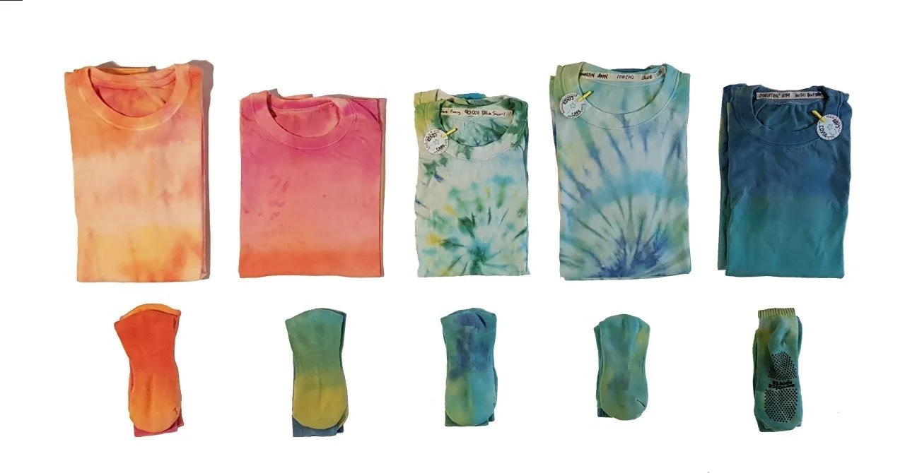 Five folded tie-dye t-shirts in different colors and five matching pairs of socks, all displayed on a white background.