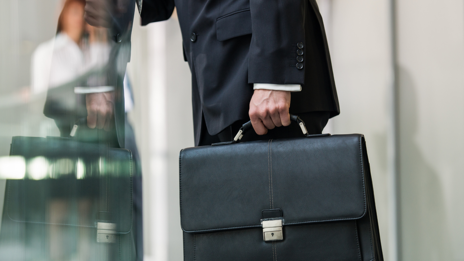 A businessperson in a dark suit holding a black leather briefcase.