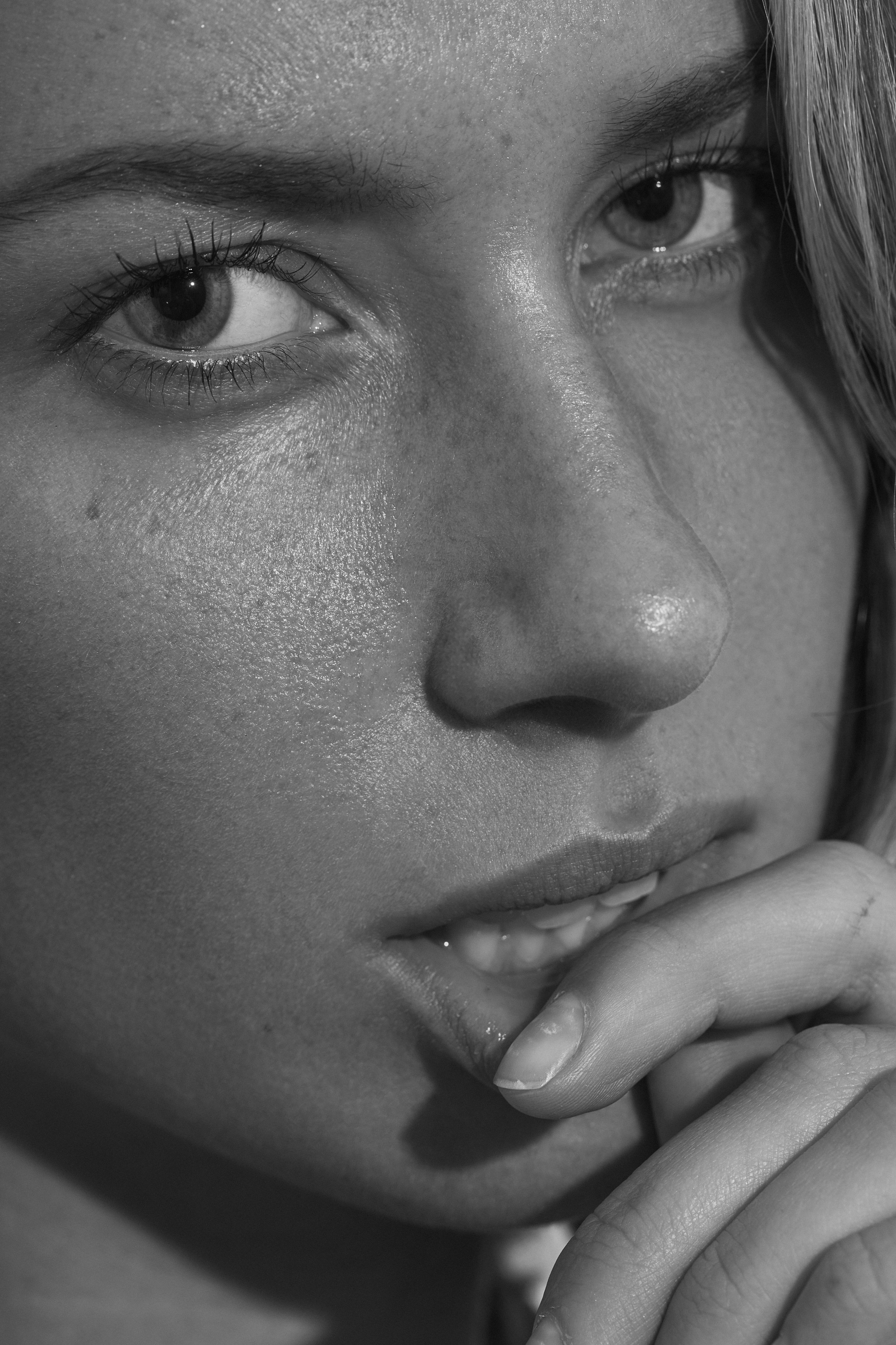Primer plano de una cara de mujer en blanco y negro, con expresión pensativa, tocándose los labios con la mano.