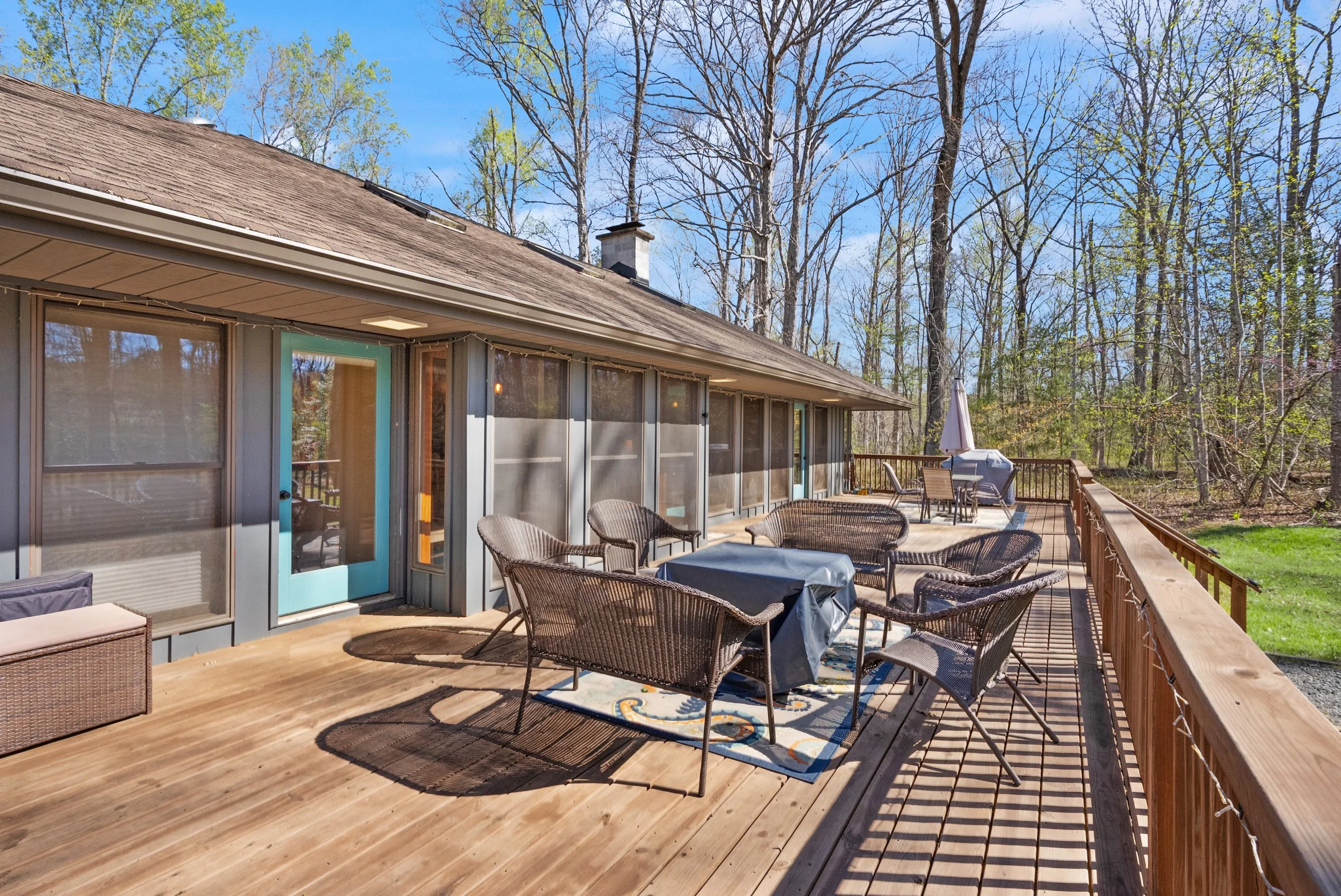Wooden deck with patio furniture and grill, surrounded by trees and a blue sky.