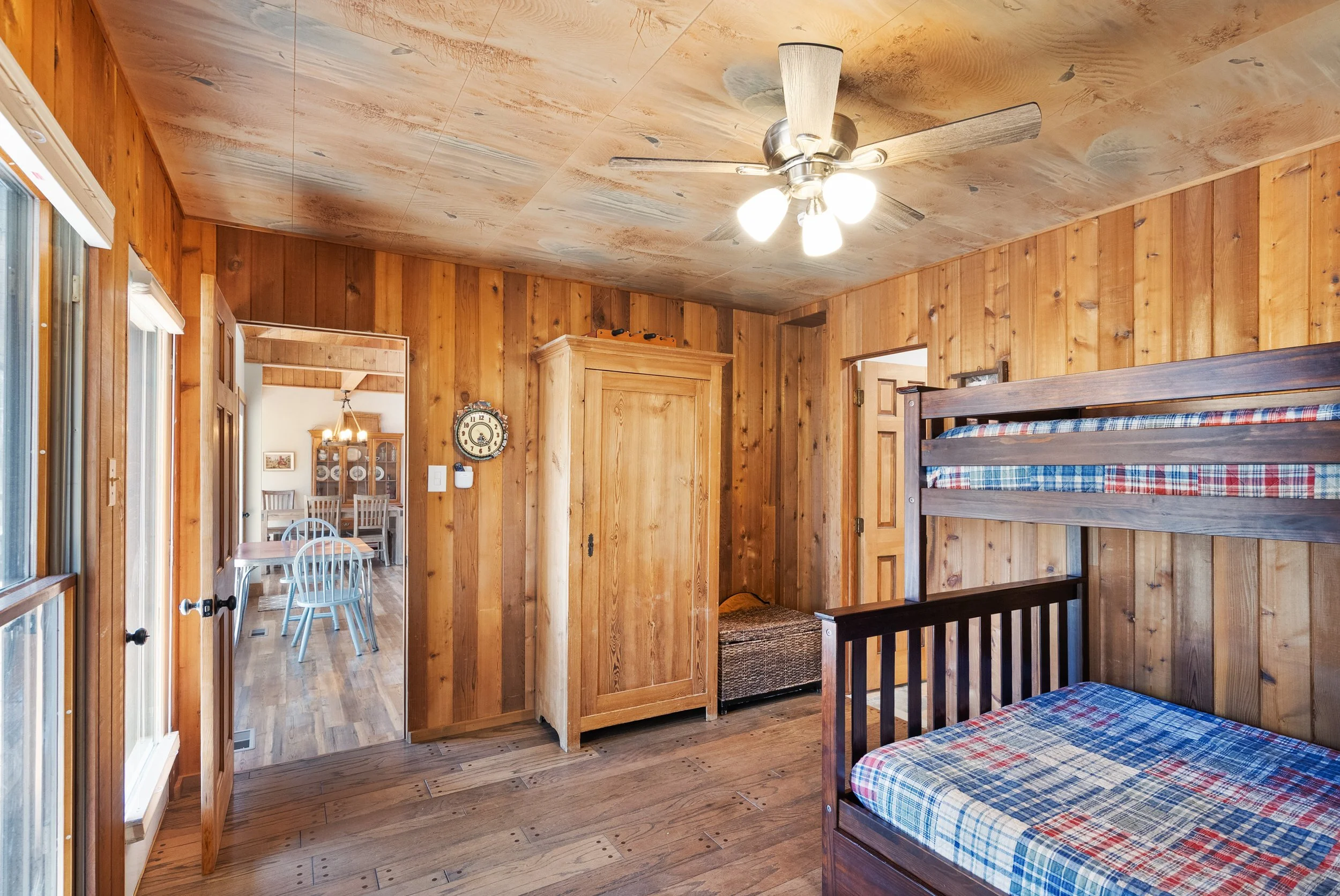 Wood-paneled bedroom with bunk beds, a ceiling fan, and a view into a dining area with light-colored wooden furniture.