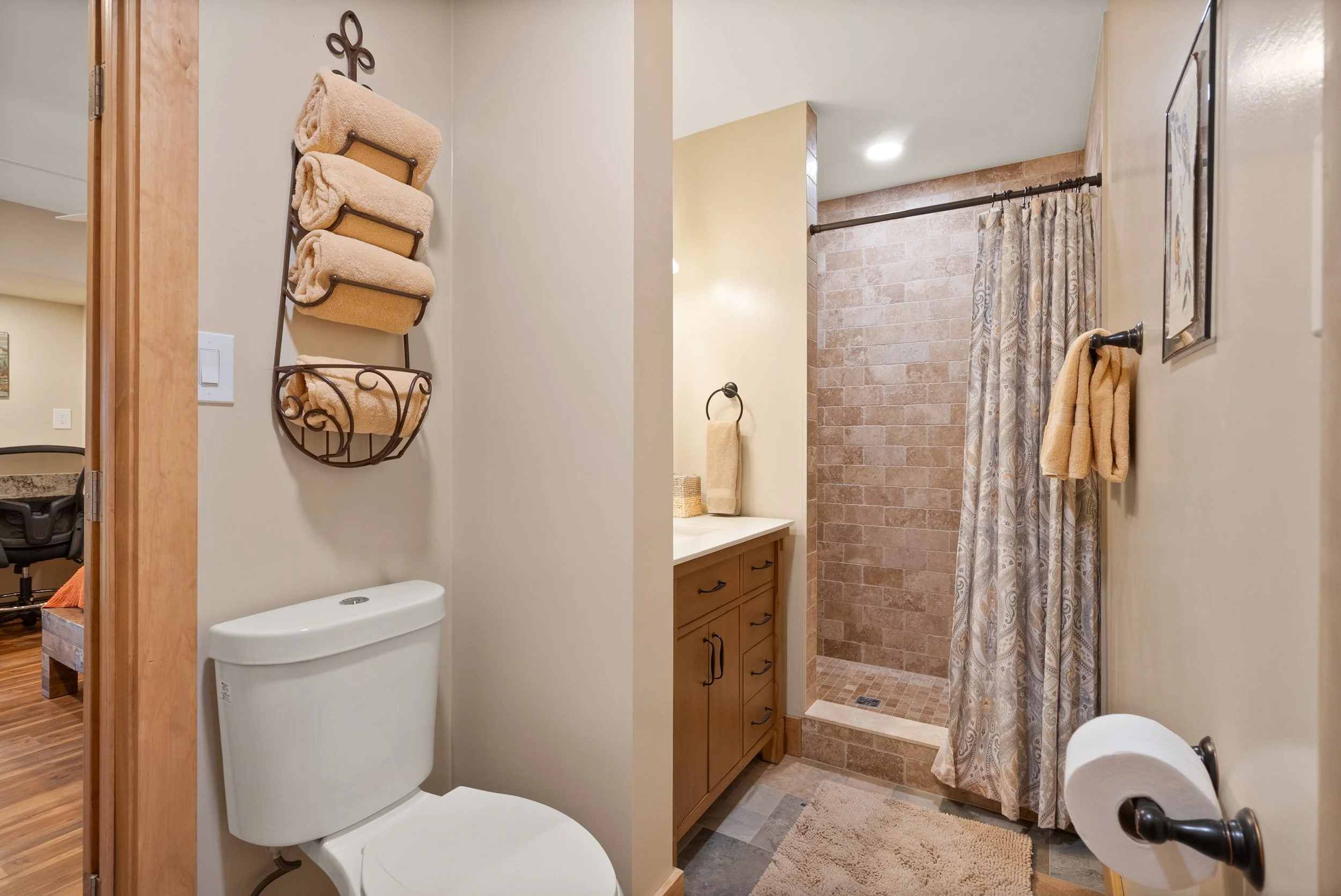 Bathroom with a white toilet, wooden vanity with a sink, and a walk-in shower with a curtain.