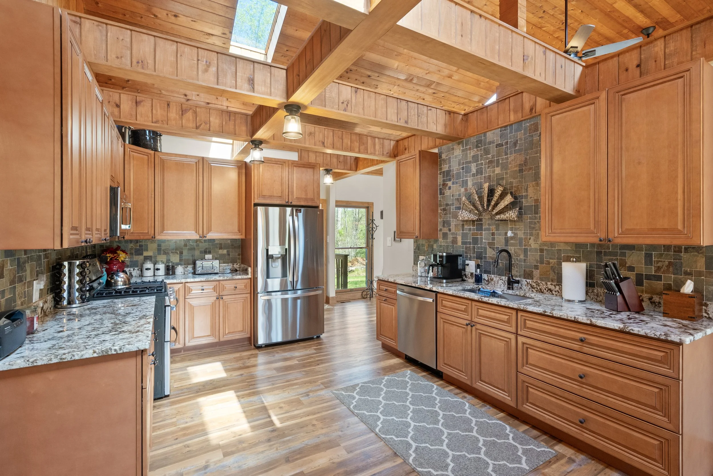 Kitchen with wooden cabinets, granite countertops, stainless steel appliances, tiled backsplash, and a wooden ceiling with skylights.