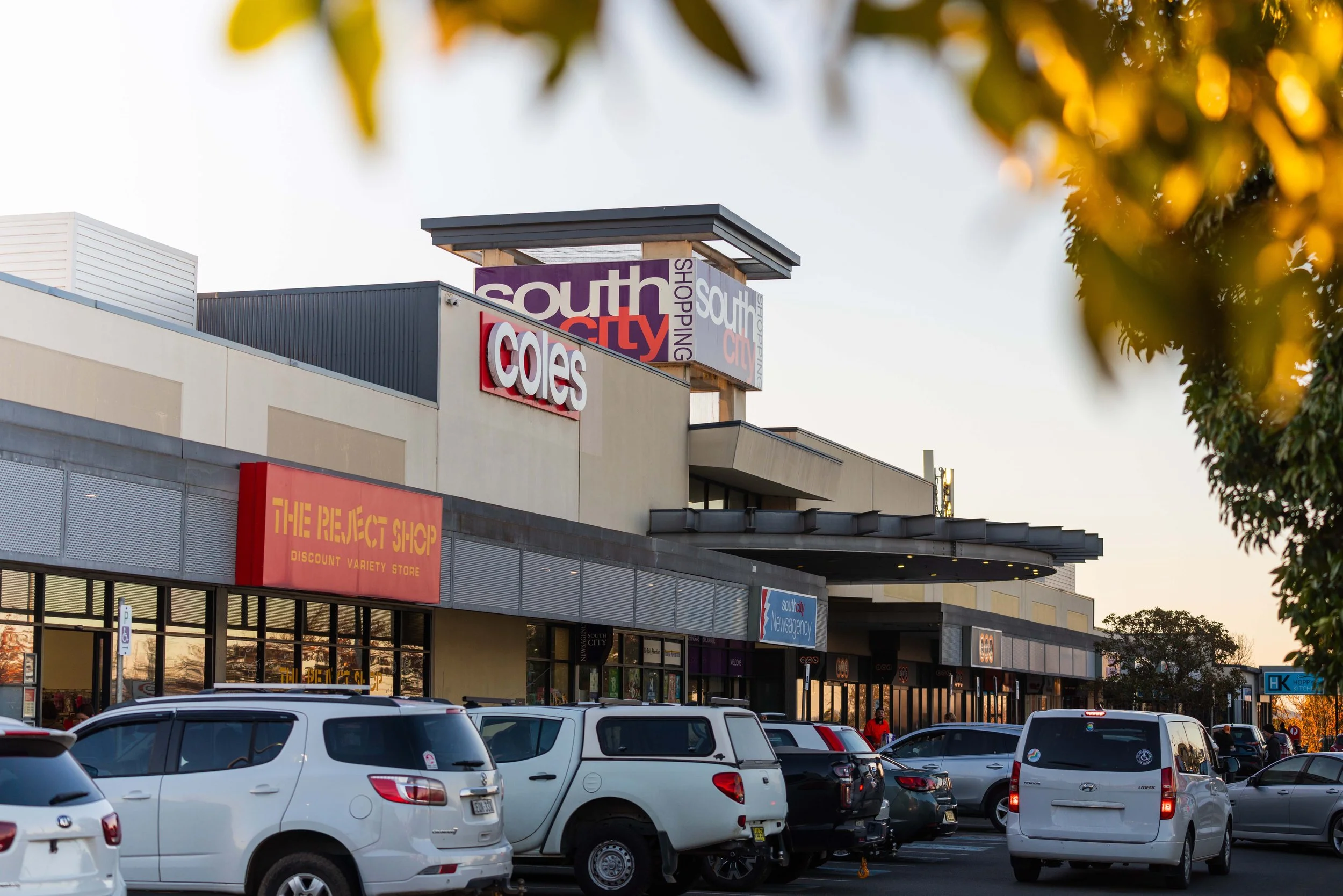 Shopping centre with stores including Coles and The Reject Shop, and a car park filled with cars.