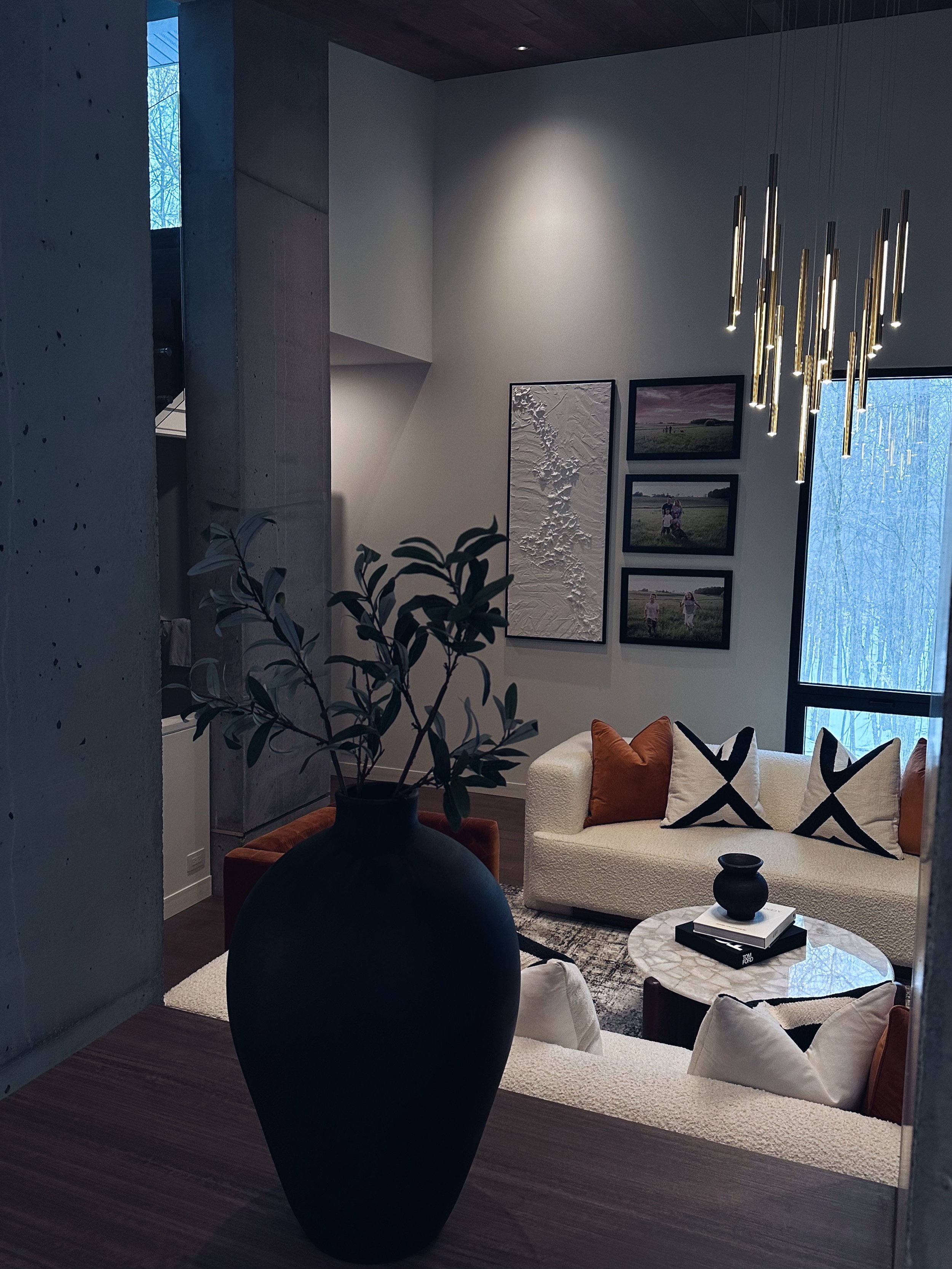 Modern living room with a white sofa, decorative pillows, a round marble coffee table, and wall art, illuminated by a contemporary chandelier.