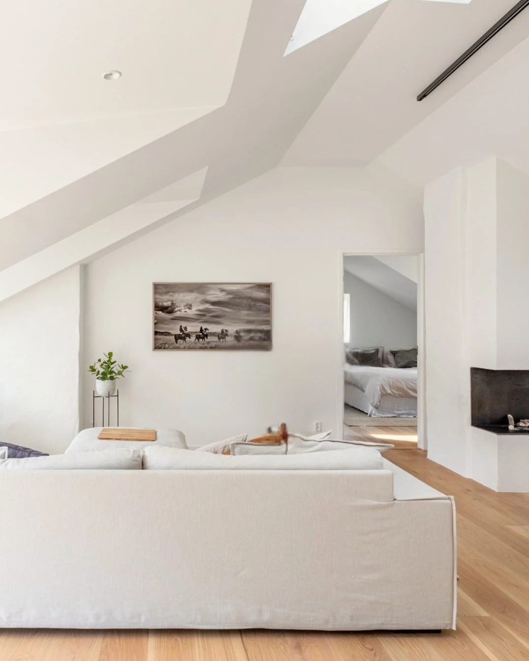 Helles Wohnzimmer mit weißen Wänden, einer Couch, Wandbild und einem Durchgang zu einem Schlafzimmer. Stimmiges modernes Wohnzimmer dank Einrichtungsberatung von Onterior - Dein Online Interior Design Studio.