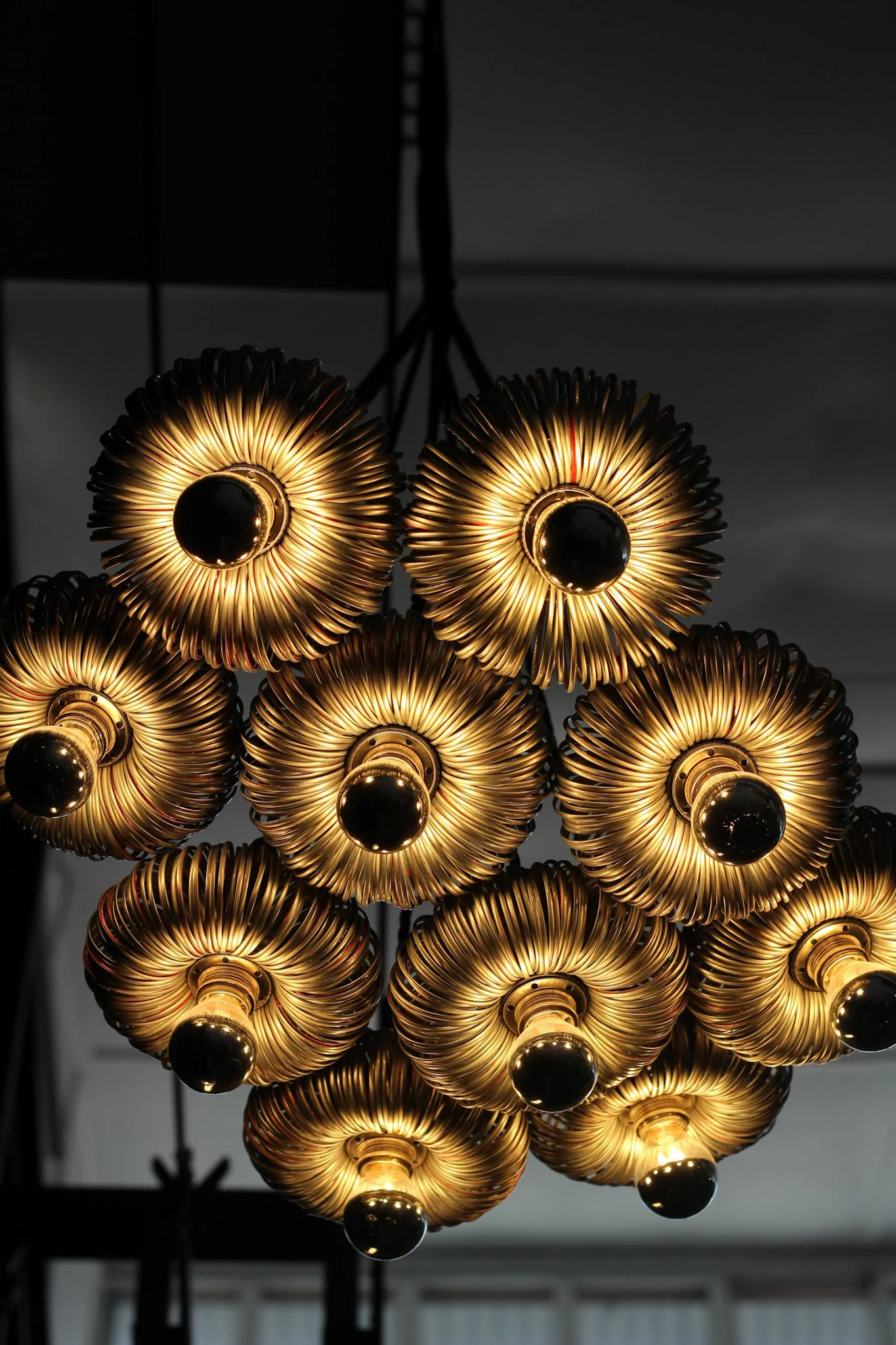 Close-up of a modern chandelier with multiple gold-colored circular light fixtures with black central spheres, hanging from black cords against a dark ceiling.