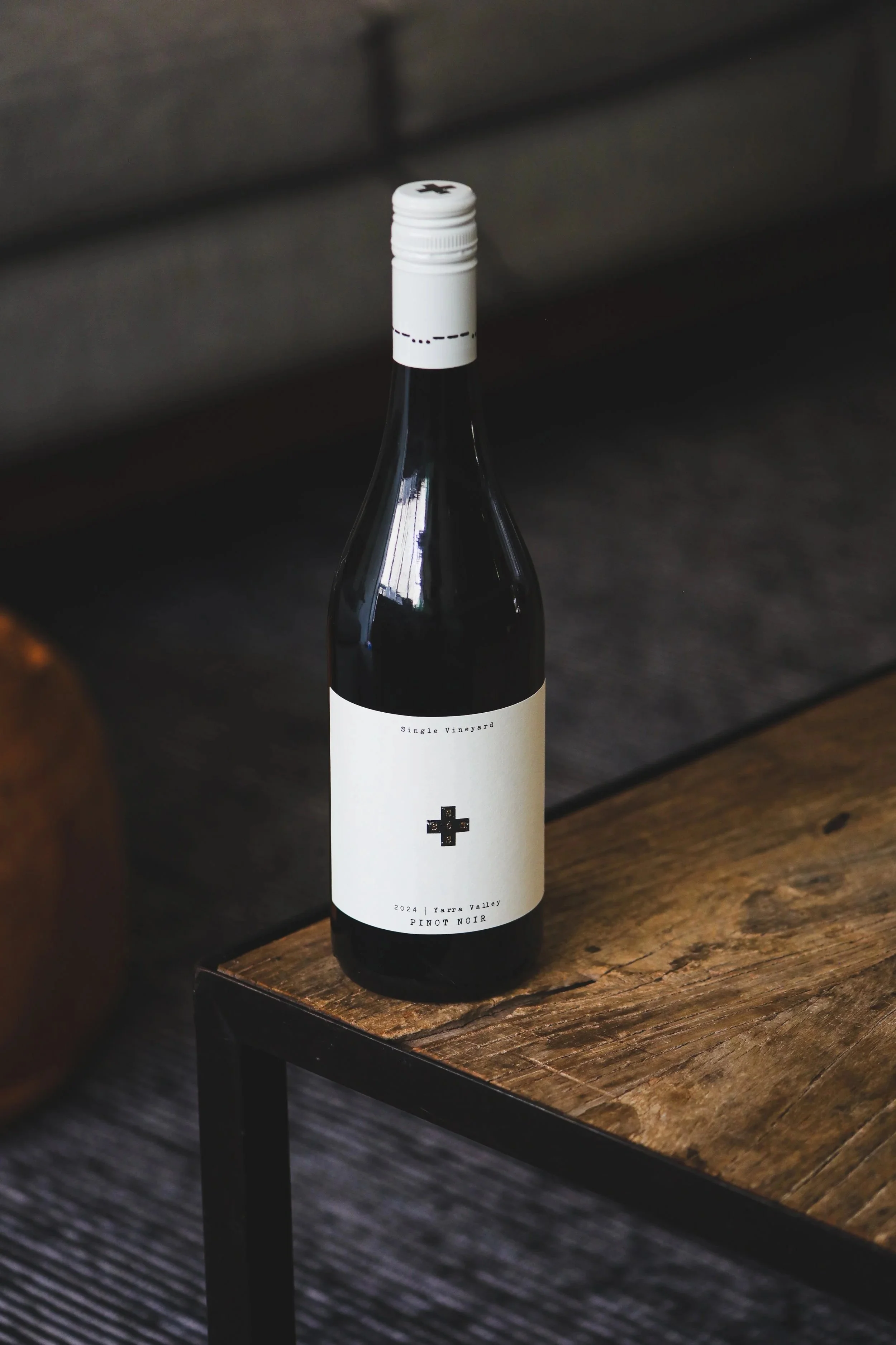 Bottle of wine with a minimalist white label reading 'Single Vineyard 2024 Yarra Valley Pinot Noir' on a wooden table.