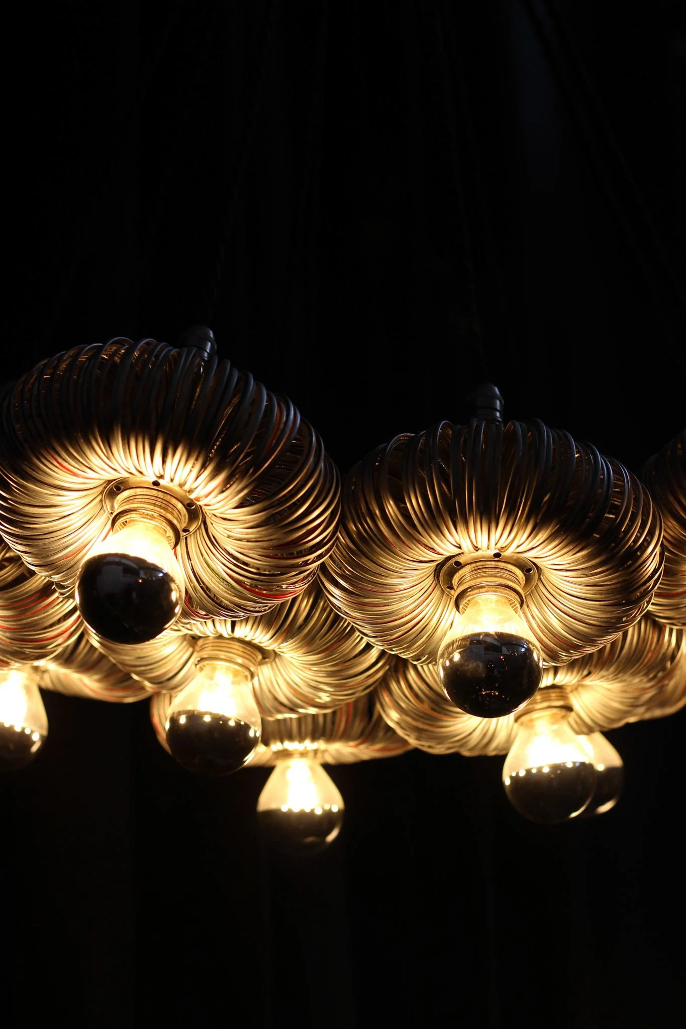 Close-up view of a modern chandelier with multiple illuminated bulbs and metallic spiral accents against a black background.