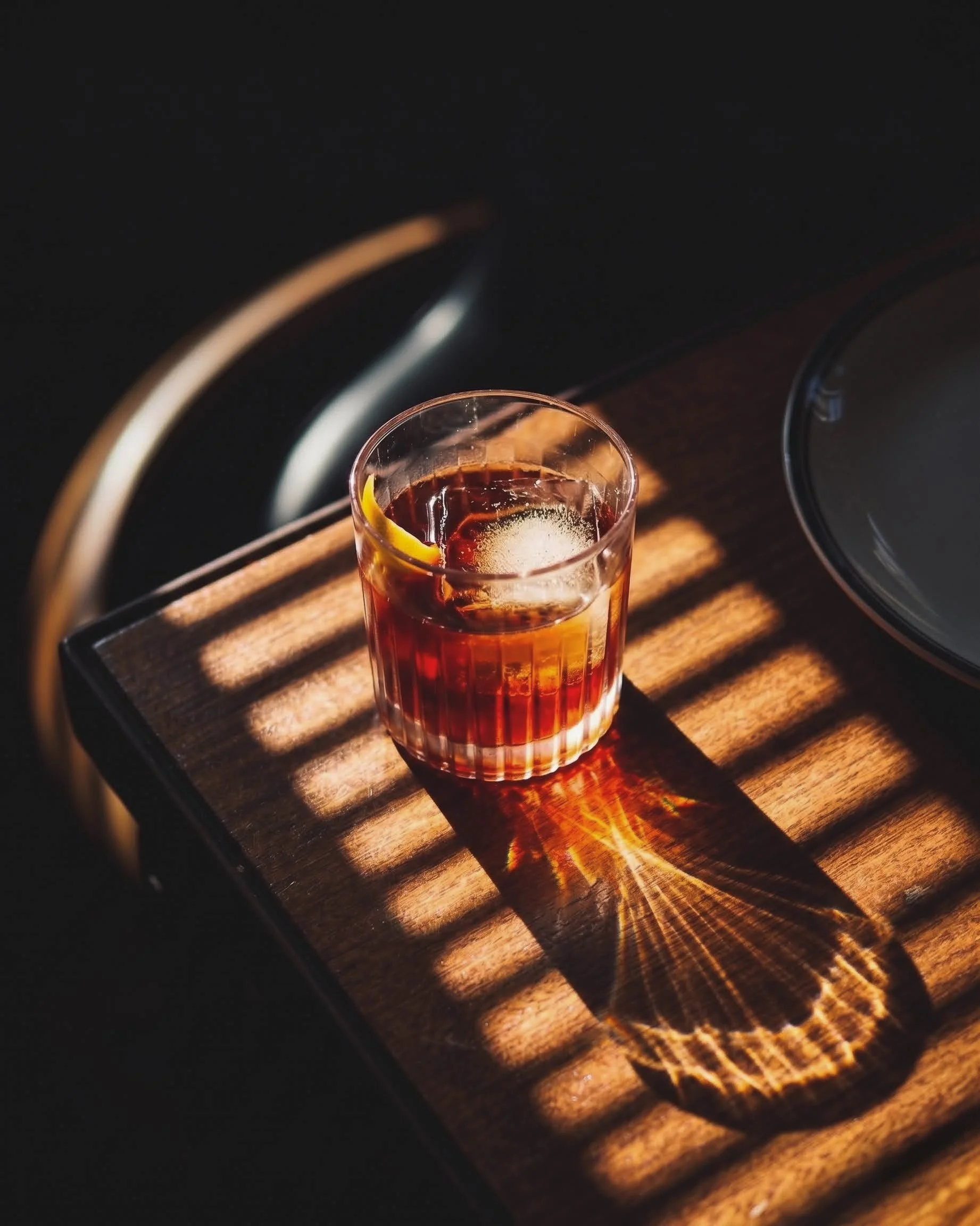 A glass of dark cola with lemon slices on a wooden tray, sunlight creating patterns on the tray.