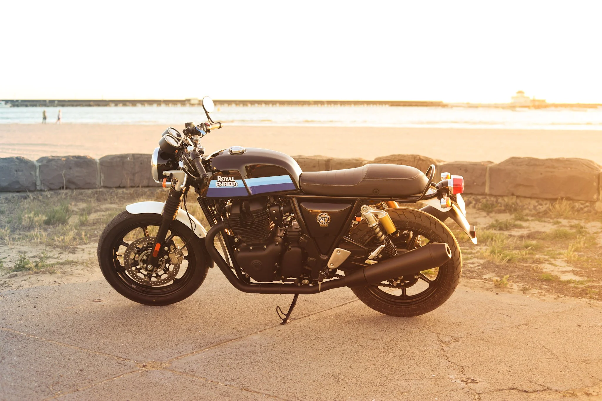 Black Royal Enfield motorcycle parked near a beach with a sunset in the background.