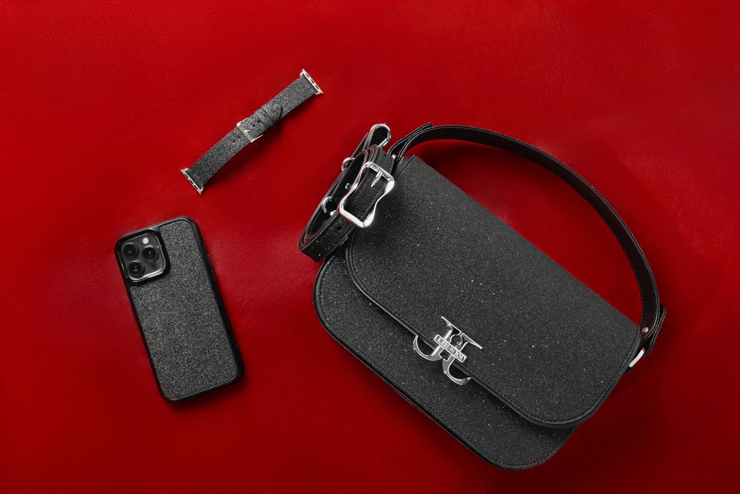 A black, glittery handbag, an iPhone with a matching glittery case, and a matching glittery watch strap on a red surface.