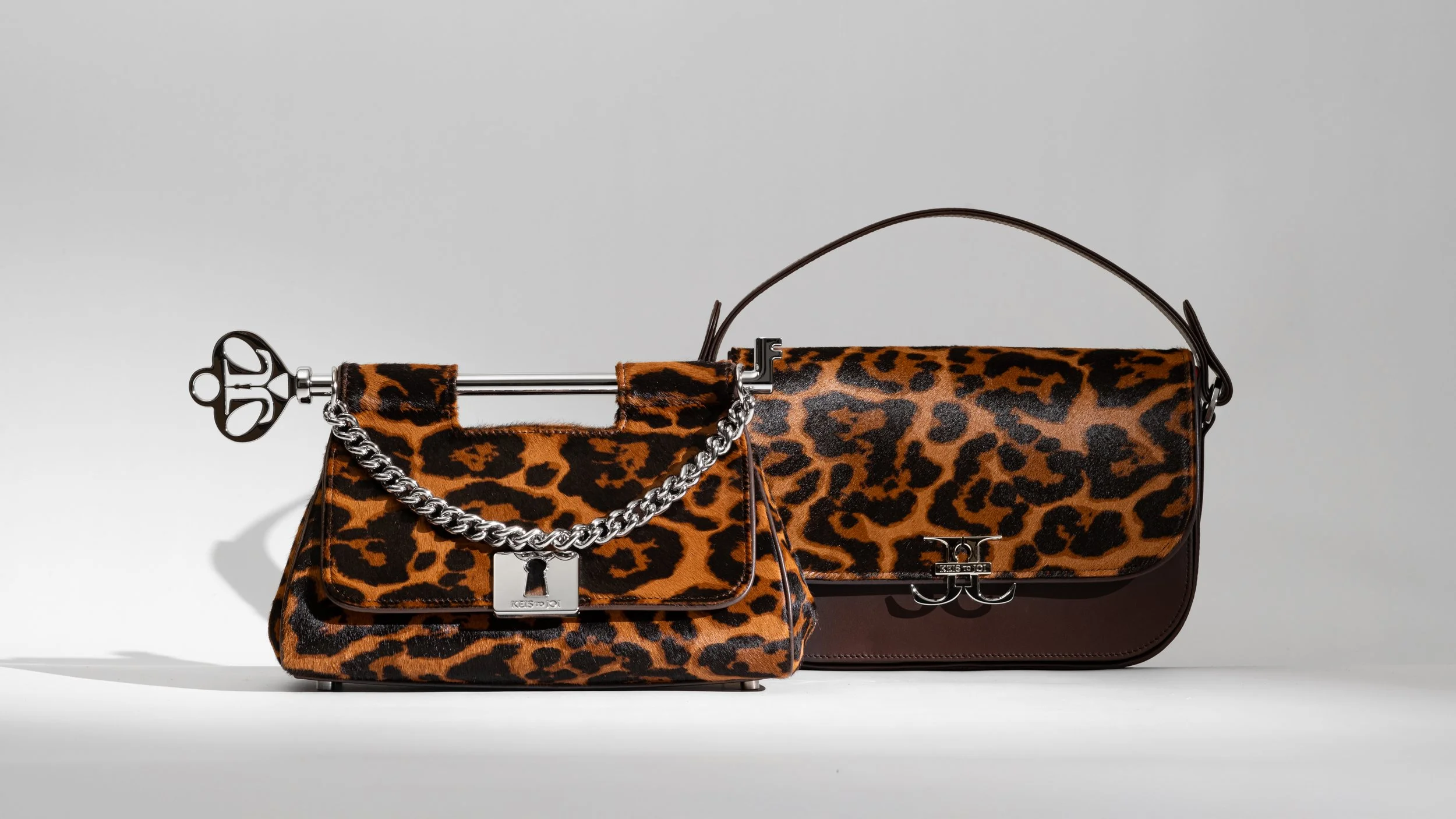 Two leopard print handbags with metal chain accents and lock details, set against a plain gray background.
