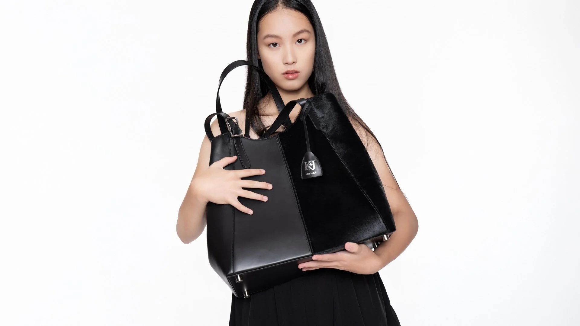 Young woman with long black hair holding multiple black handbags against white background.