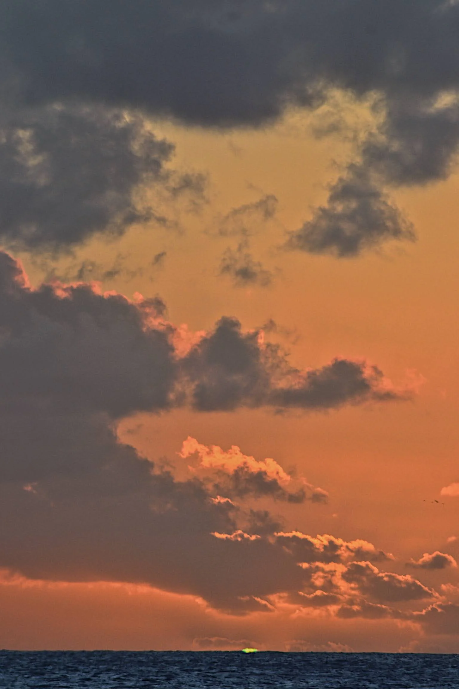 Sunset over the ocean with dark clouds and a bright orange sky.