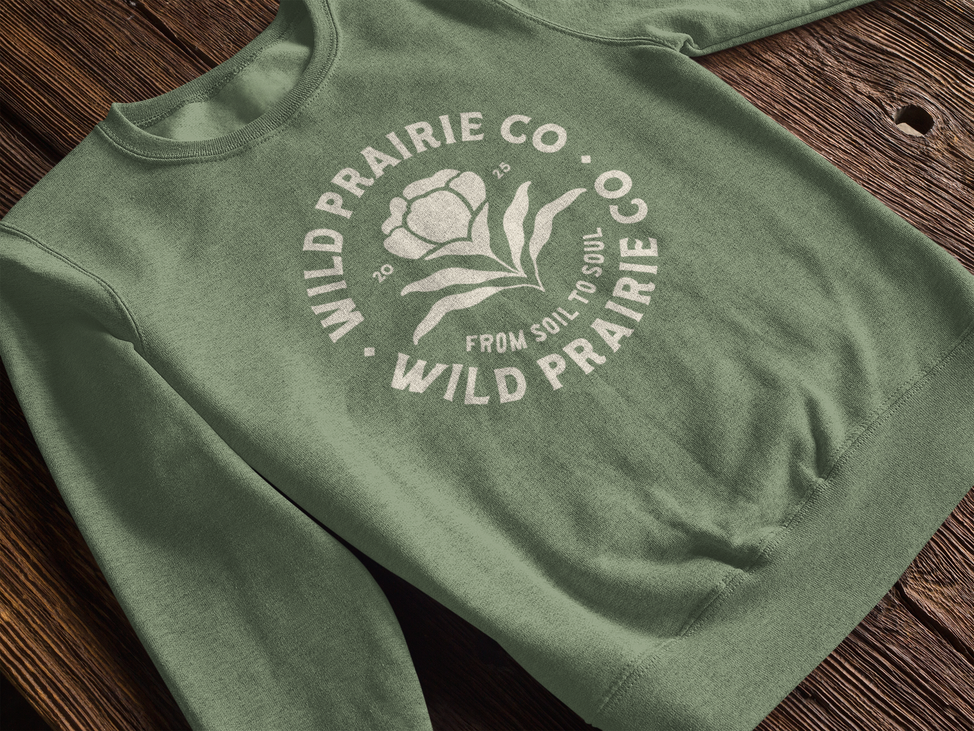 Green sweatshirt with white logo and text, laid flat on a wooden surface.