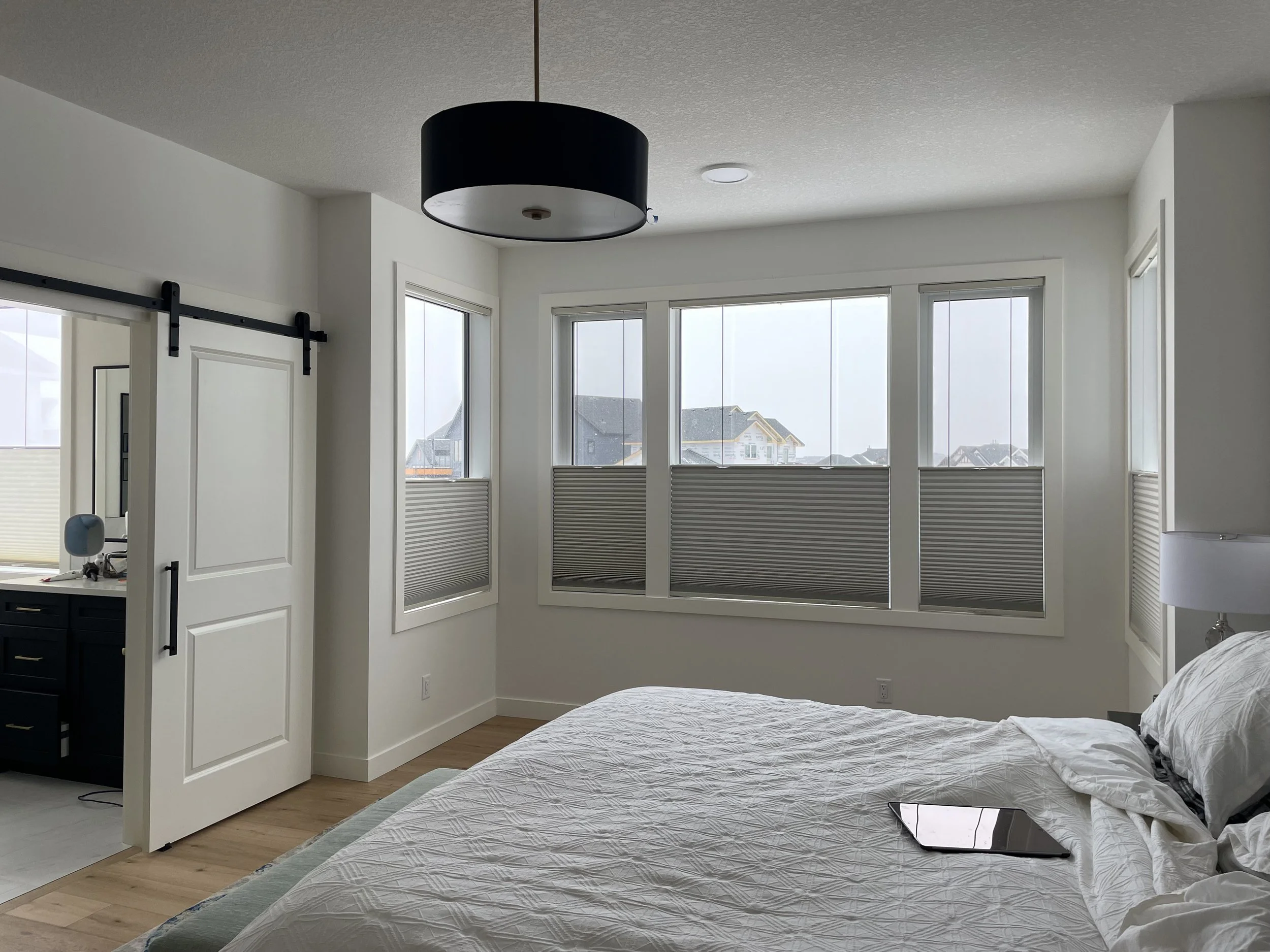 Bedroom with large windows, white bedding, and a tablet on the bed.