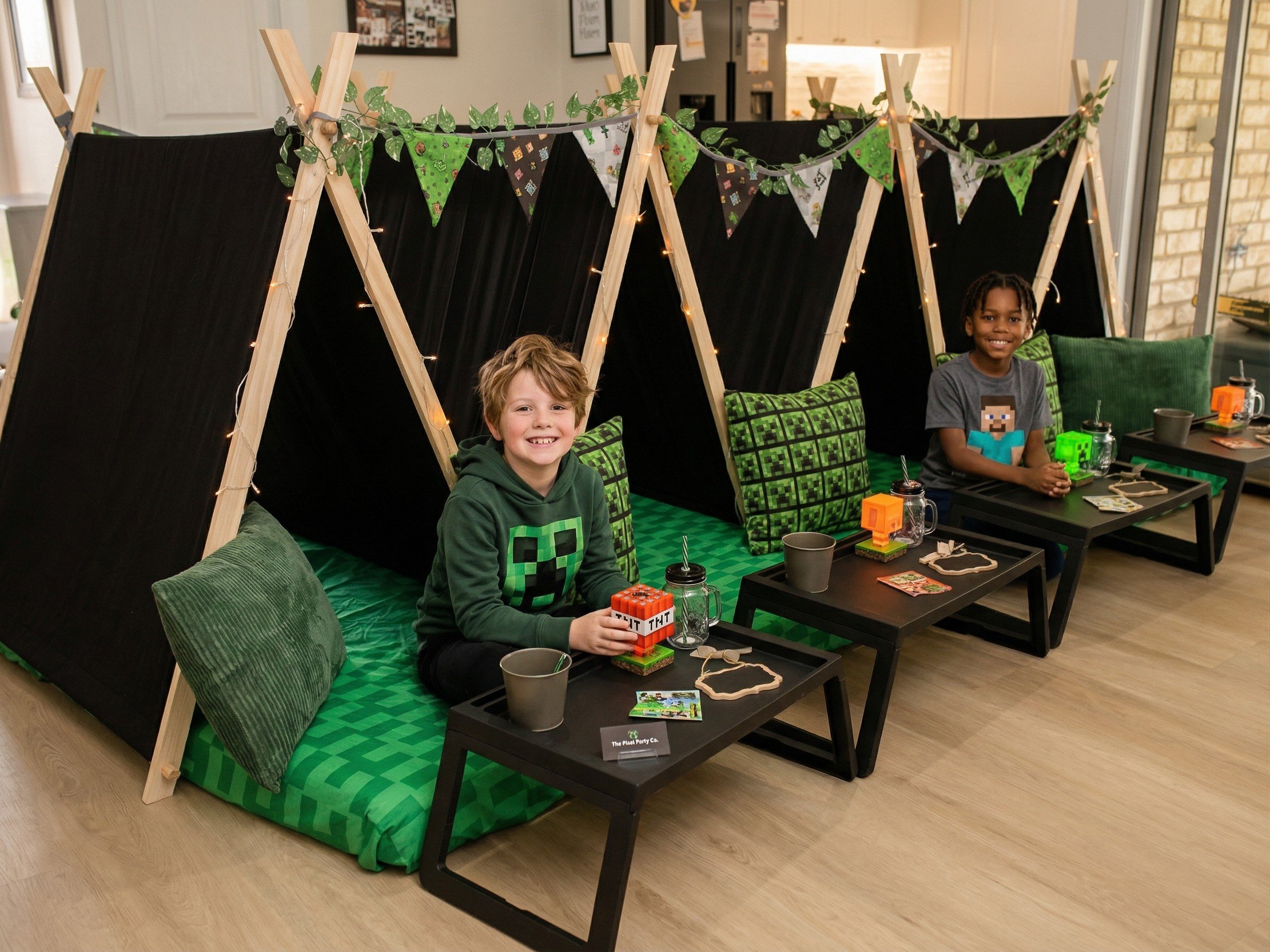 Two children sitting in Minecraft-themed teepee tents with green cushions, gaming-themed decorations, and snacks during a kids sleepover birthday party.