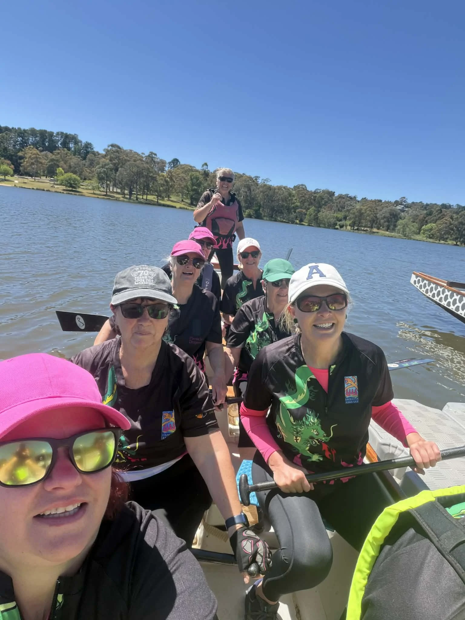 Training session for Orange Pinnacle Dragon Boat Club -with a group of young people paddling a dragon boat together on lake Canobolas during autumn, with colourful trees in the background.