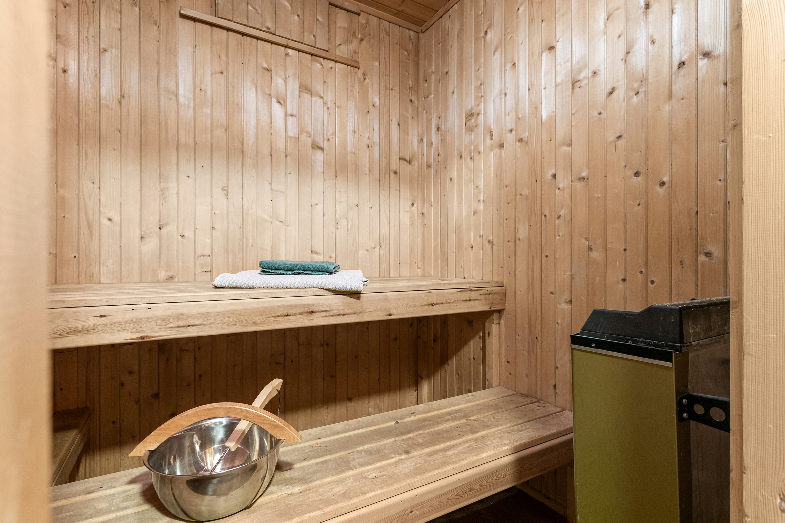 Wooden sauna interior with benches, folded towels, a ladle, and a metal stove.